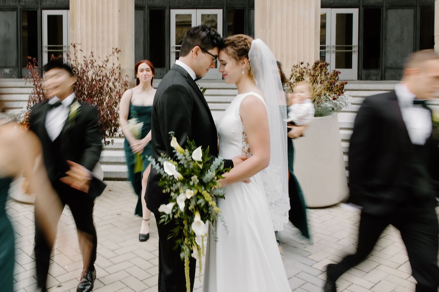 Wedding party poses together on elegant stone steps with white columns and dark bridesmaids dresses.