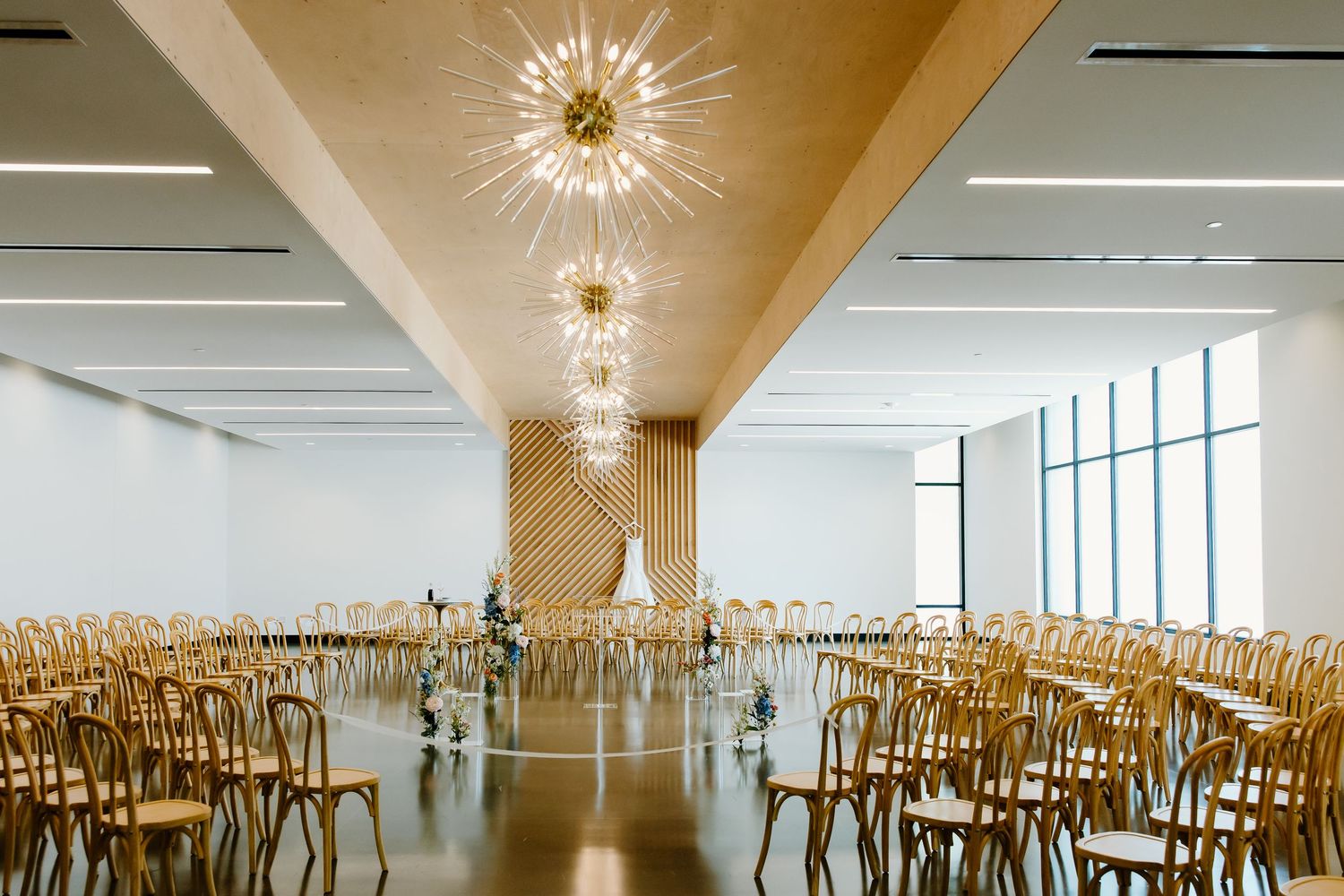 Modern banquet hall with elegant starburst chandeliers and wooden chairs arranged in neat rows.