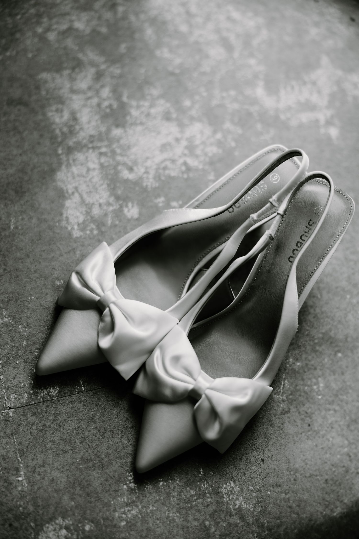 Elegant gray satin heels with bow detail photographed on textured surface.