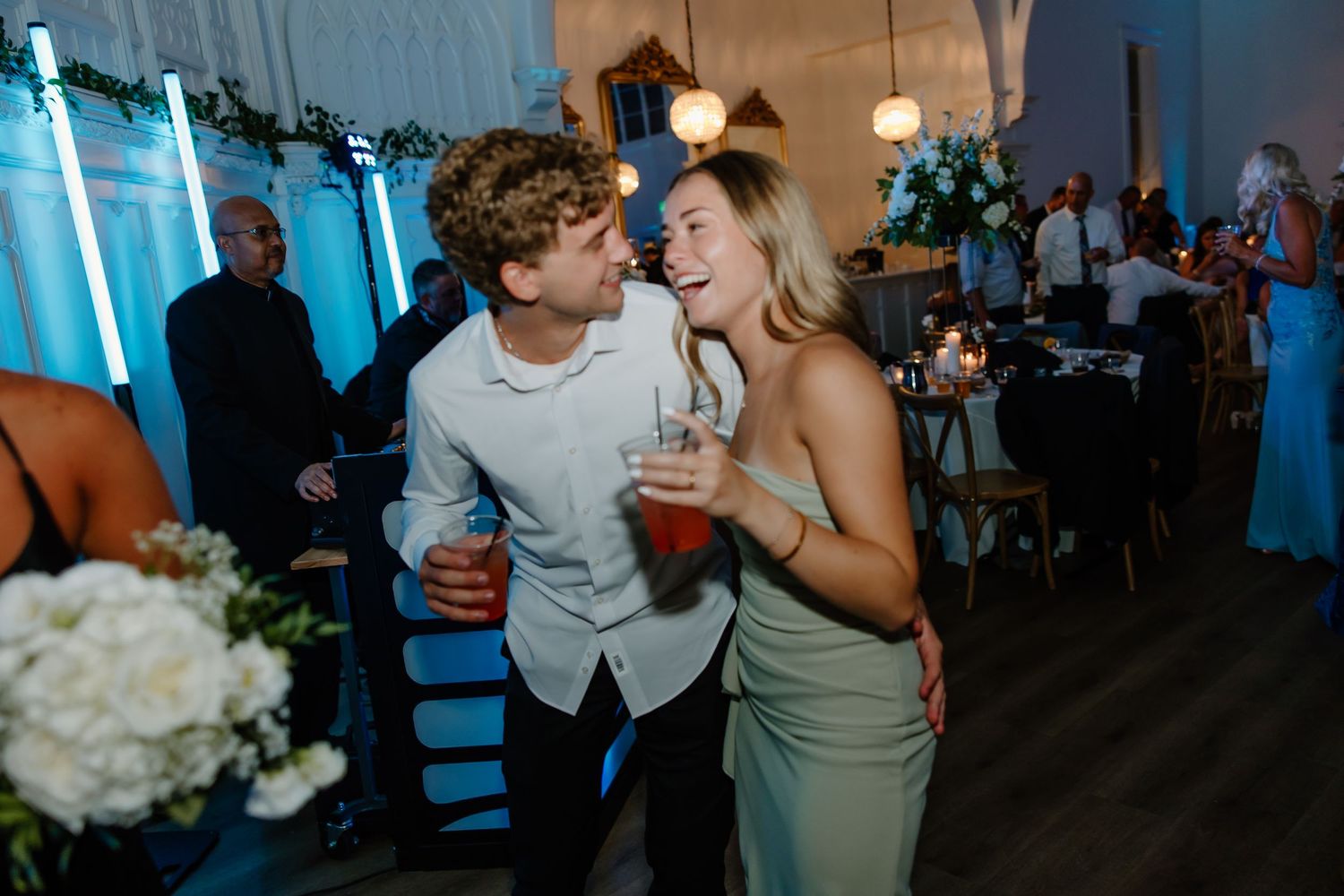 Wedding reception guests dancing and celebrating on a dance floor illuminated by blue lighting.
