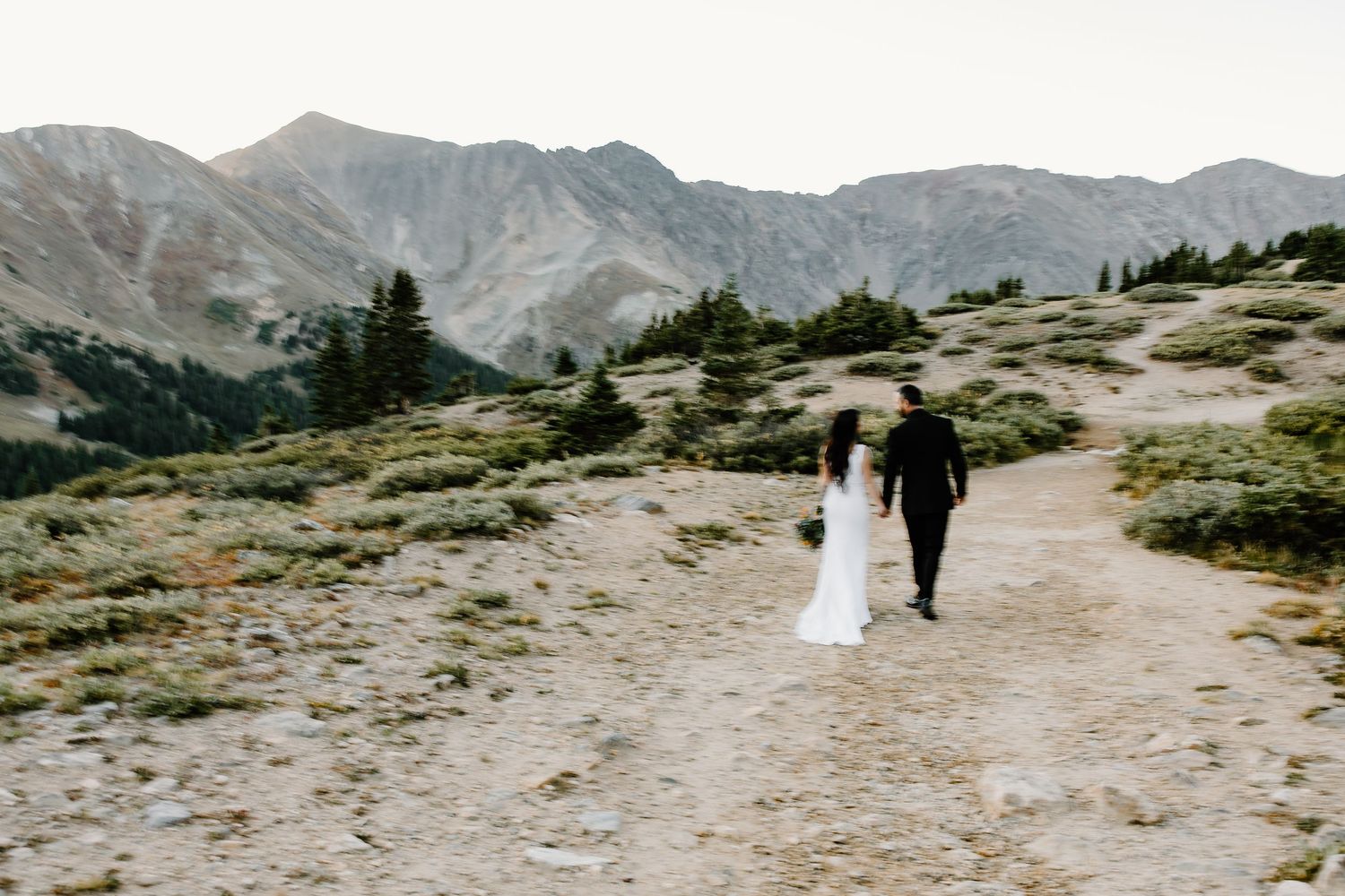 Wedding couple walking along mountain trail with scenic alpine views.
