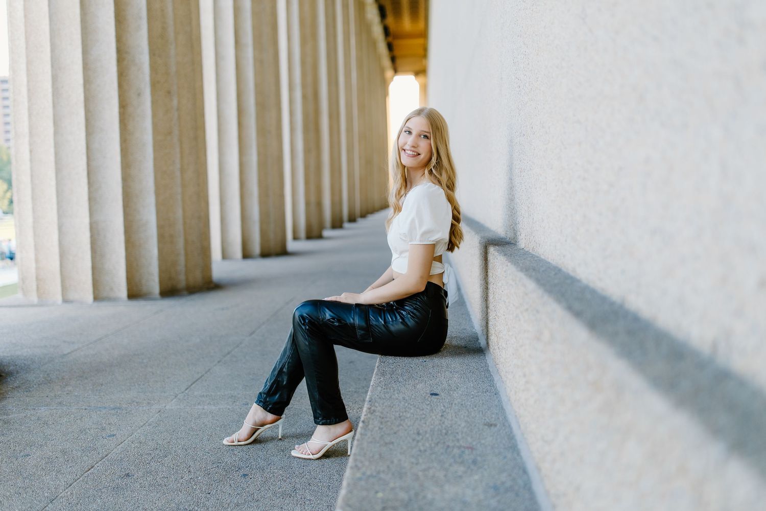 Woman in white dress sits elegantly against a modern architectural column wall in an artistic photoshoot.