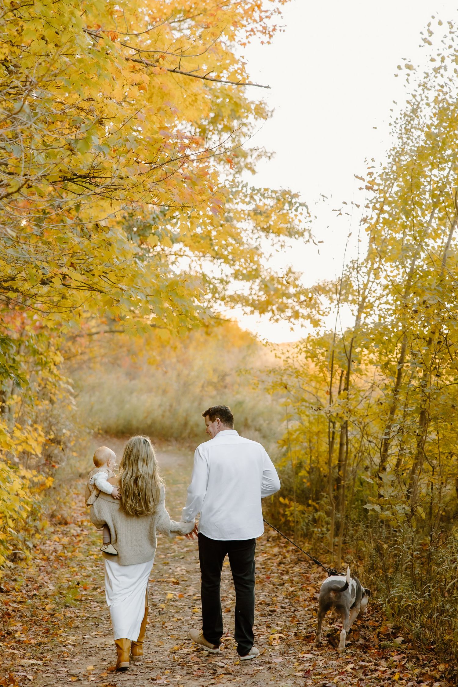 Family walking together on path surrounded by golden fall trees at sunset.