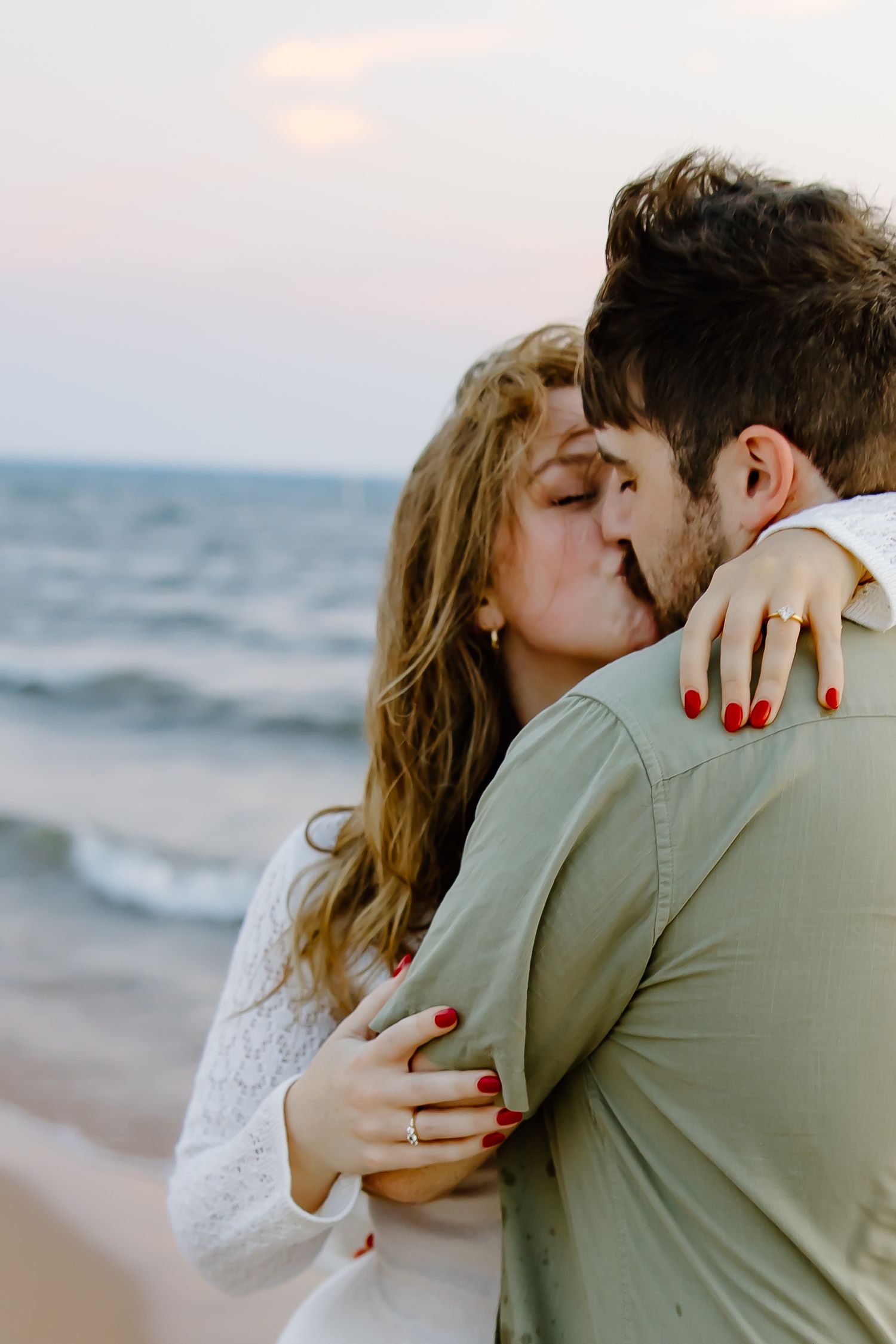 Romantic beach embrace with ocean waves and sunset in the background.