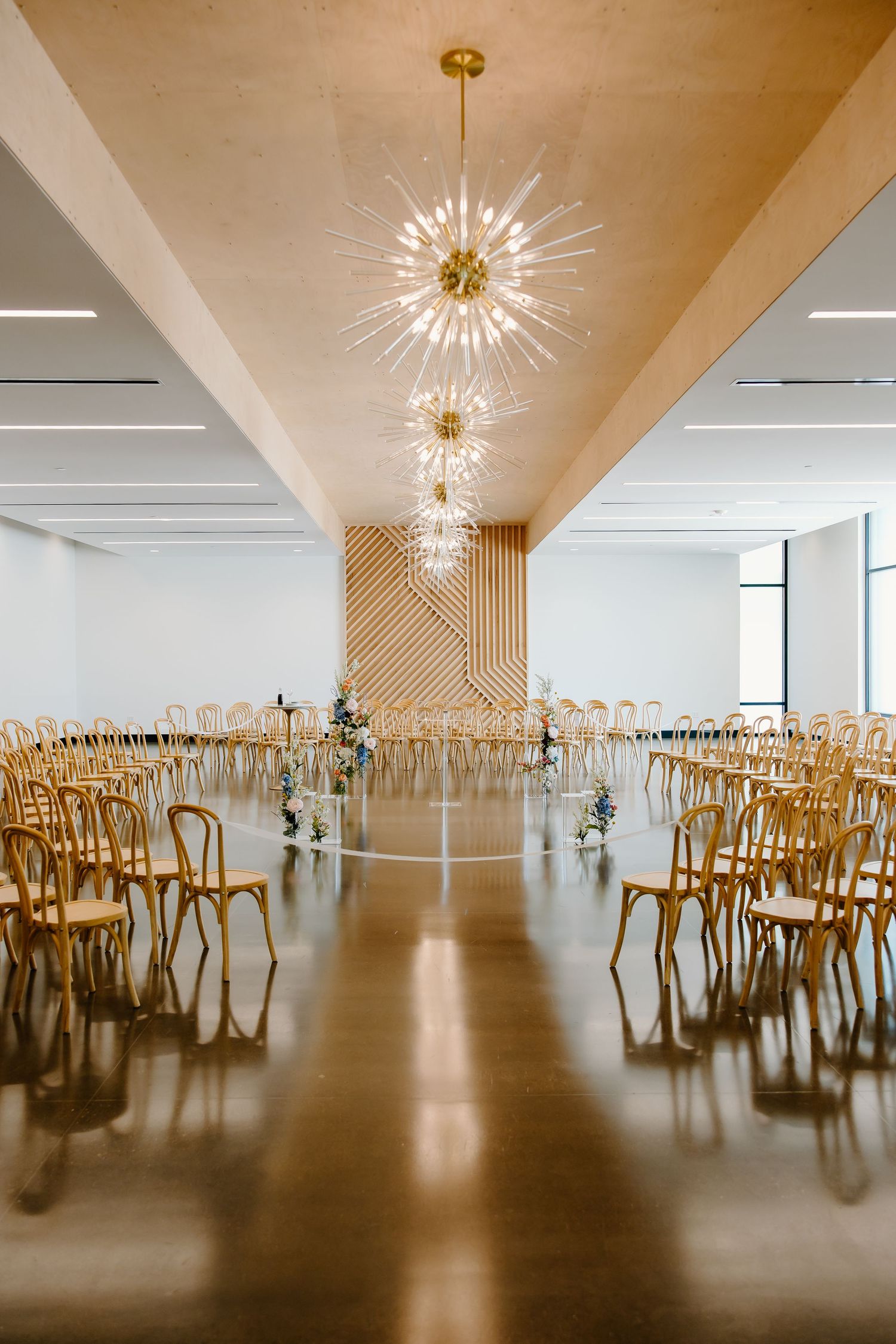 Spacious reception venue with wooden chairs and dramatic starburst lighting fixtures on the ceiling.