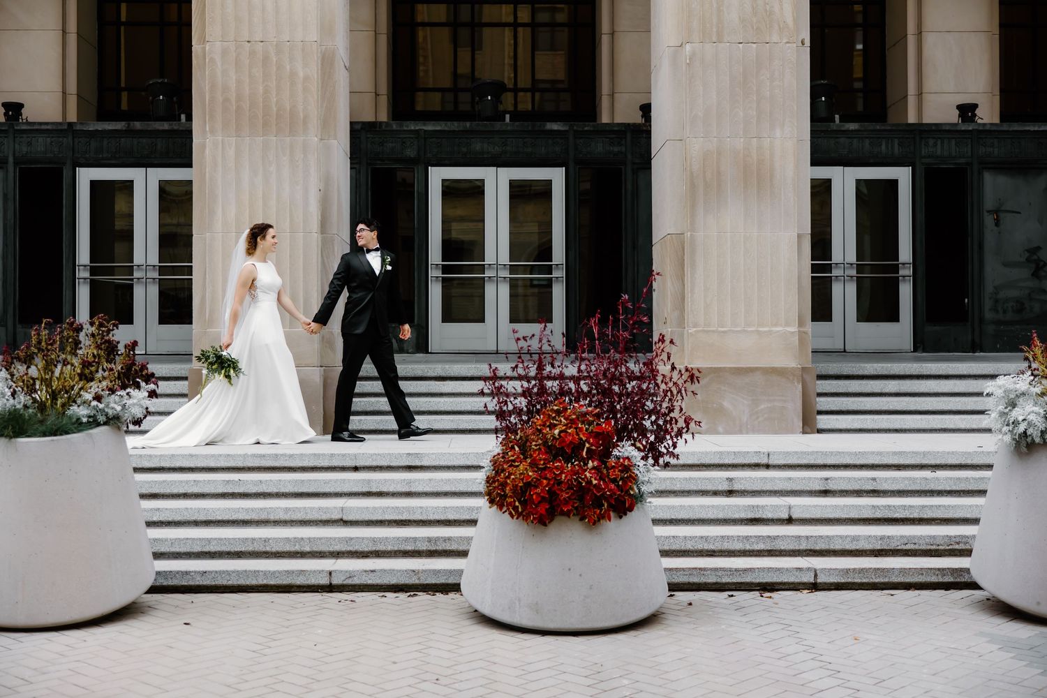Wedding couple poses in front of grand stone colonnade with white architectural details.