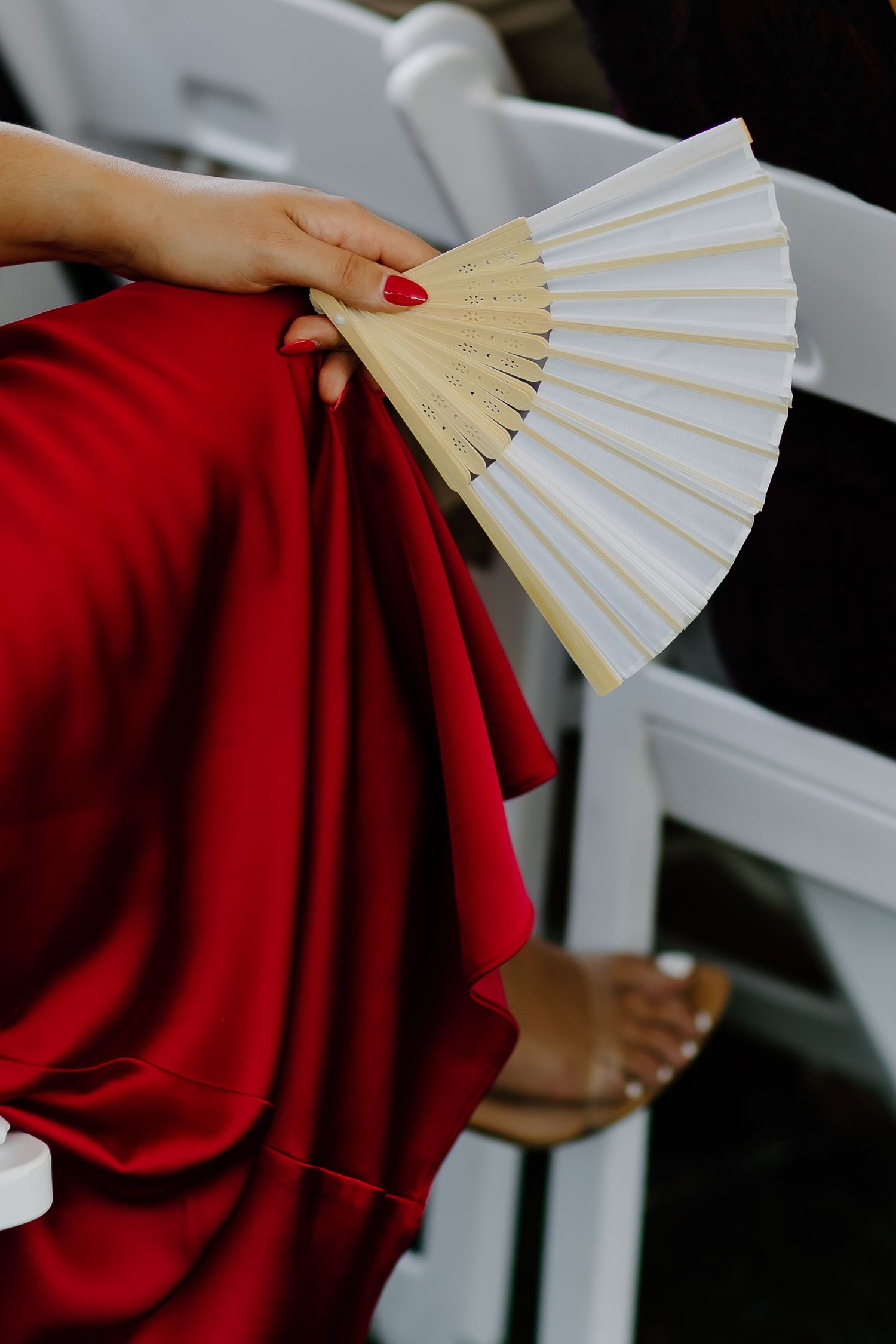Hand holding white paper fan against red fabric in elegant detail shot.