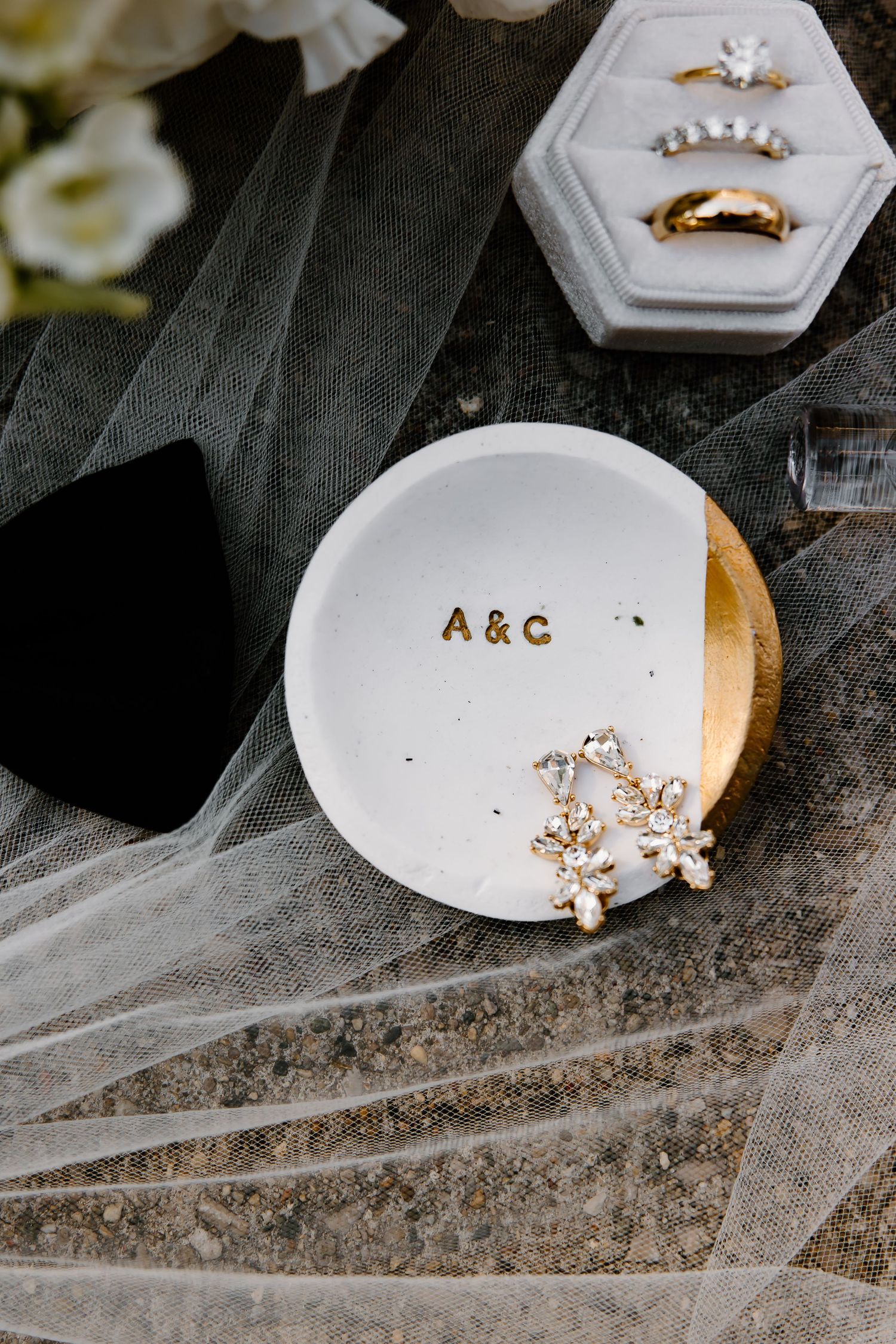 Wedding rings and jewelry displayed on a decorative white dish with initials.