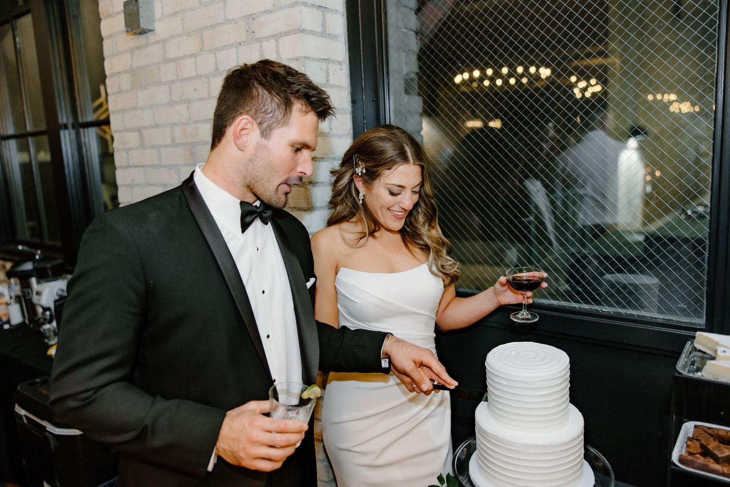 Newlyweds cutting their white tiered wedding cake at the reception.