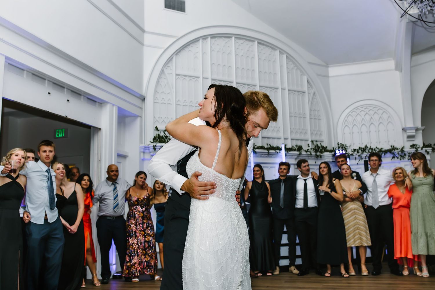 Wedding celebration in an elegant white venue with arched windows and dancing guests.