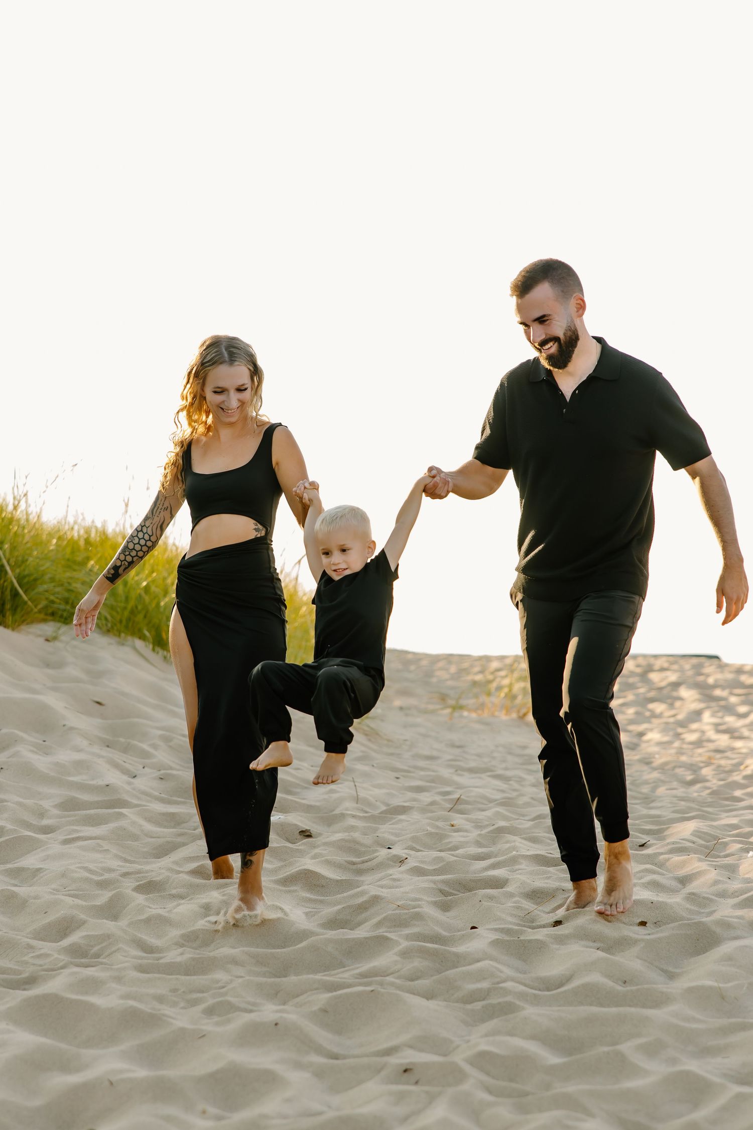 Family walking up steep sand dunes together wearing black outfits.