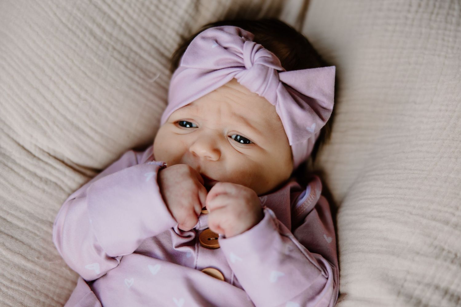 Close-up shots of an infant in purple clothing lying on white linens.