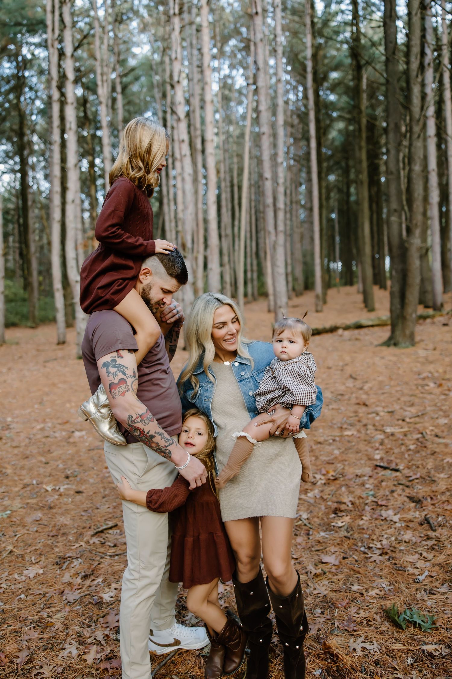 A playful family photoshoot in a pine forest with casual fall outfits and natural lighting.