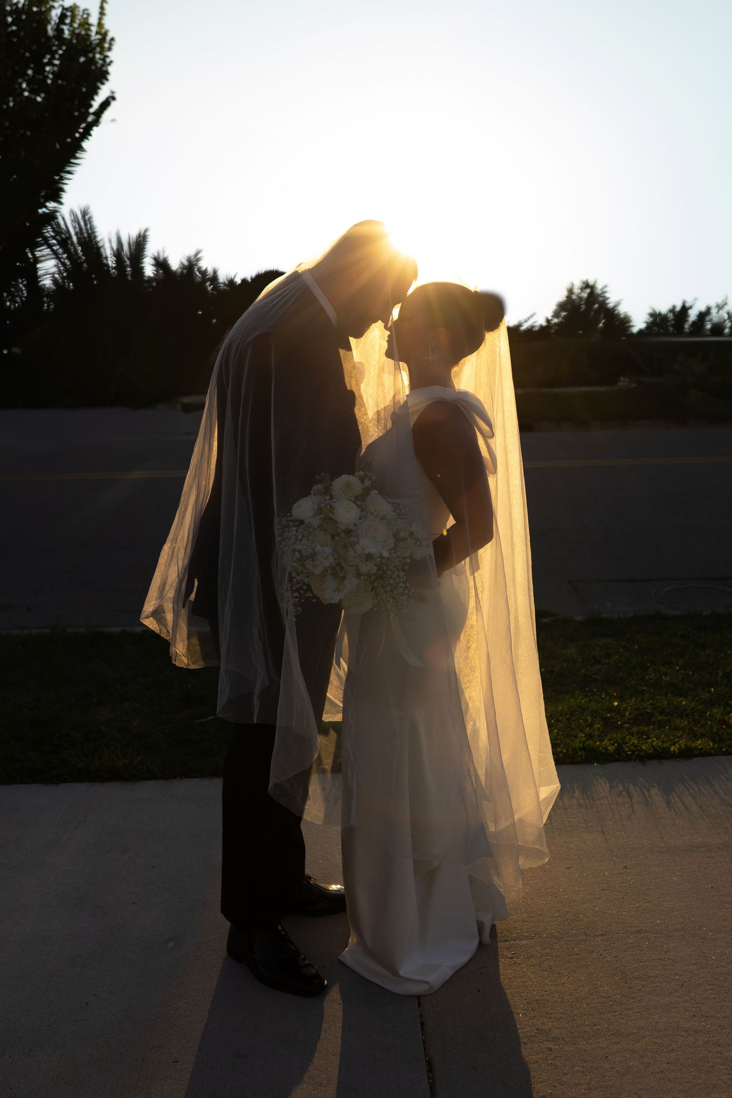 Romantic sunset wedding portrait with bride's veil flowing in golden light.