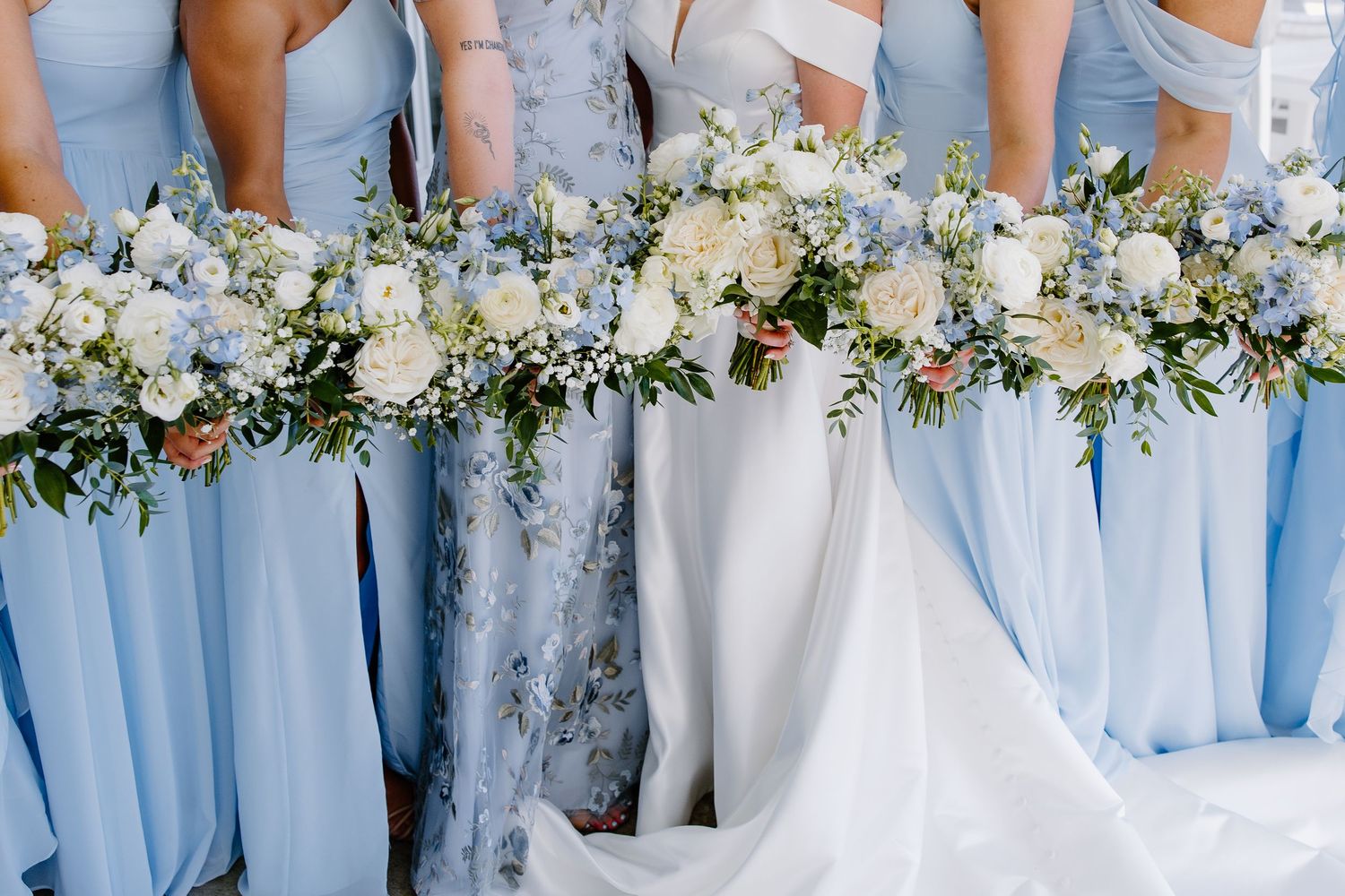 Row of bridesmaids holding white and green floral bouquets against light blue dresses.
