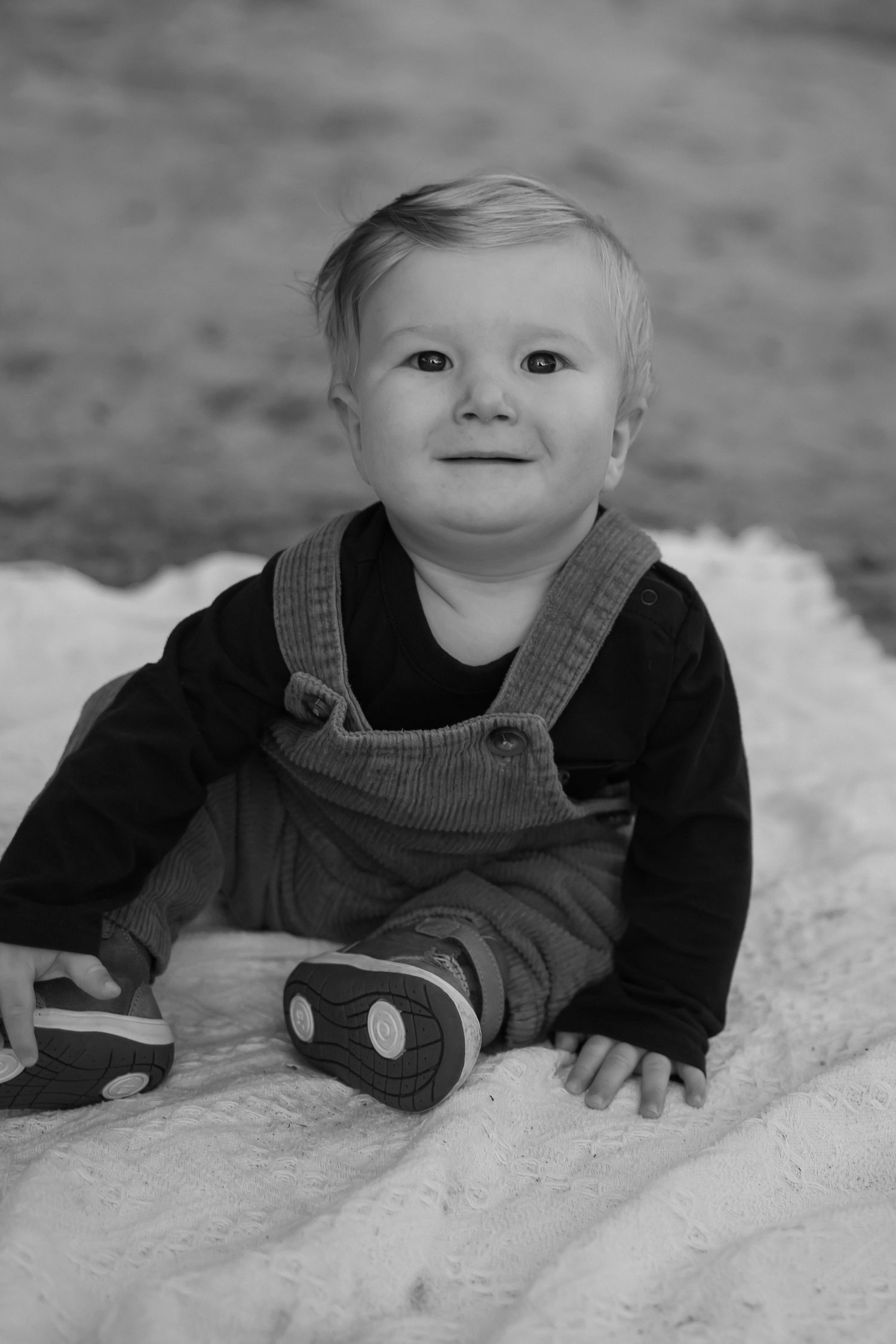 Black and white portrait of a baby in overalls on a white blanket.