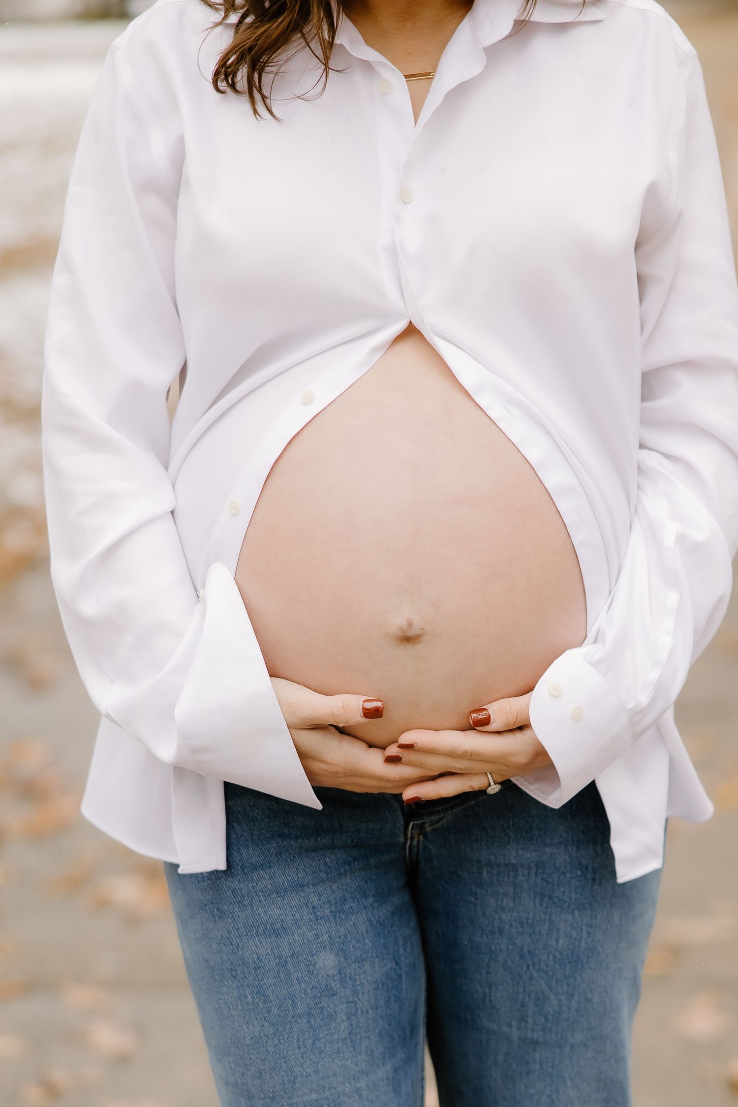 Close up of pregnant belly with white button-down shirt and jeans in winter setting.