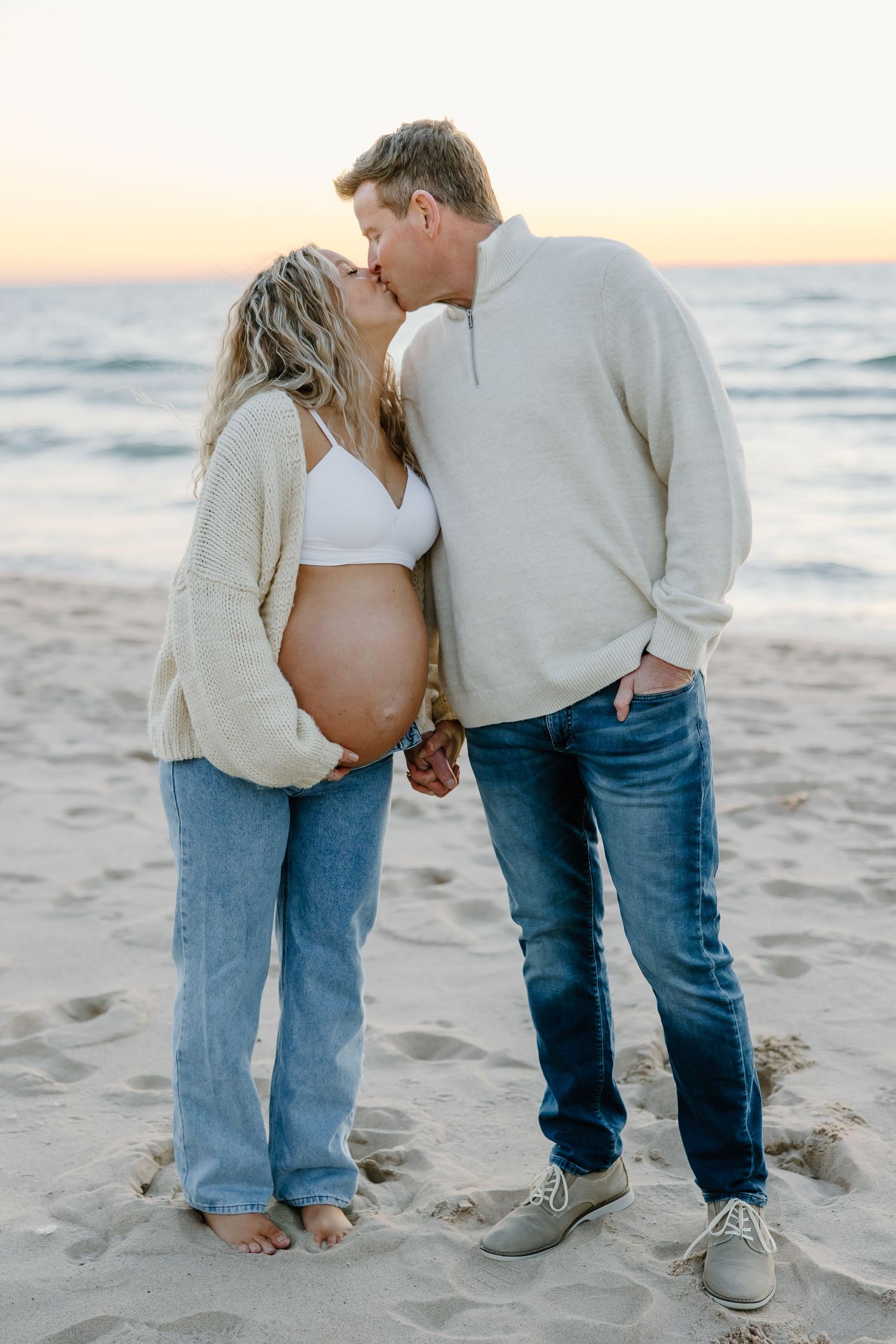 Couple in casual attire embracing on a beach during sunset.