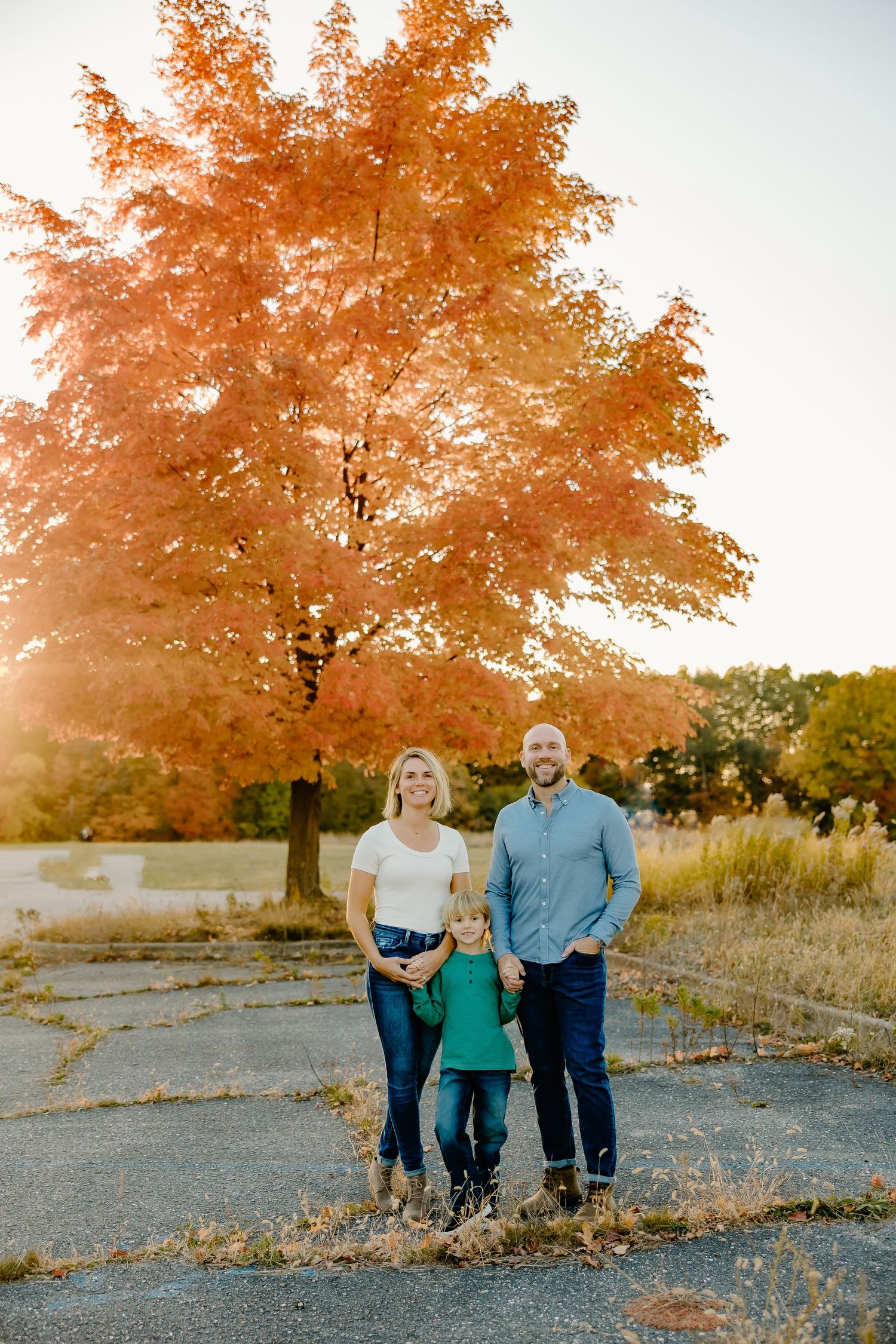 Sunset photo of a family standing together under a large orange maple tree in autumn.