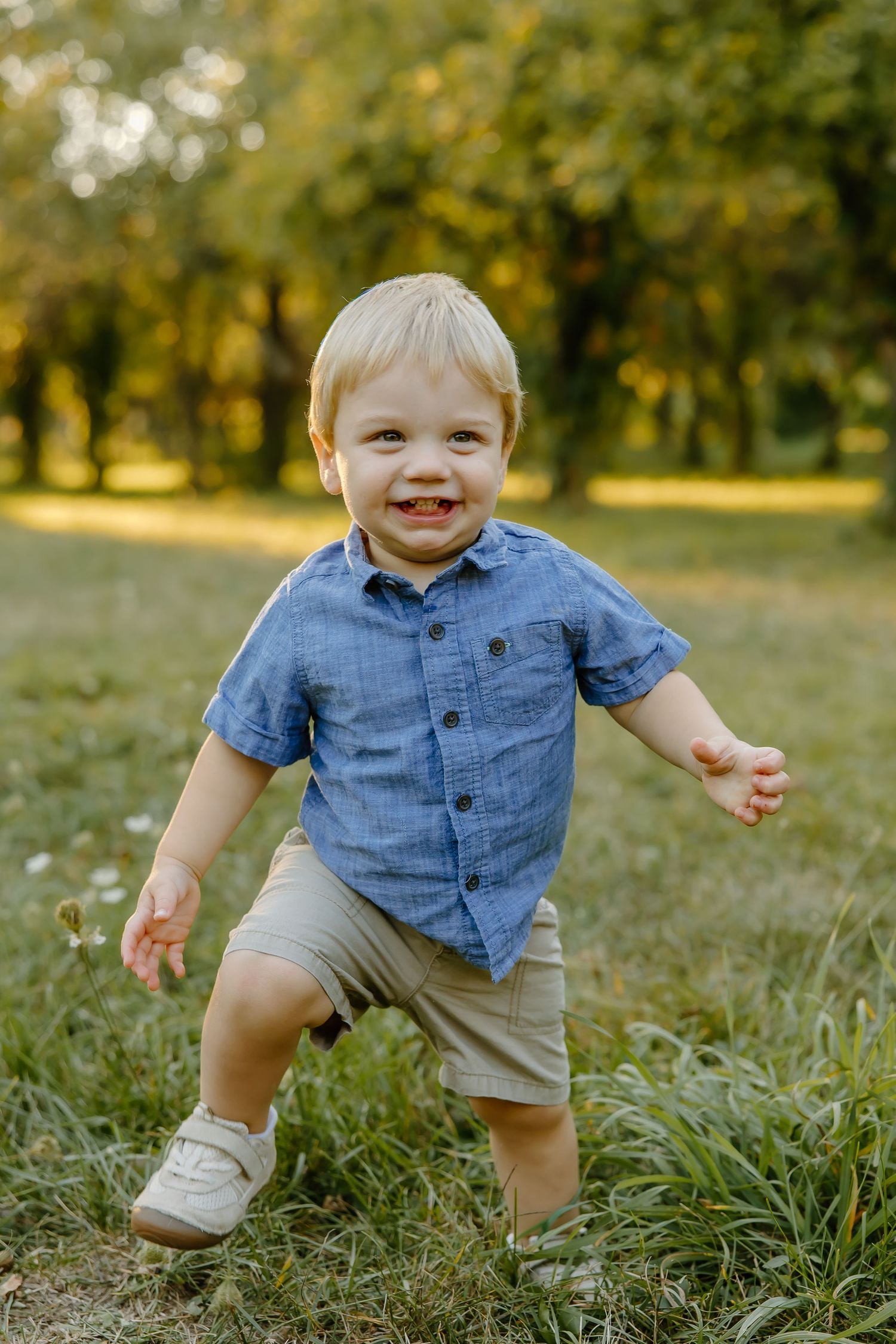 Small child in casual attire takes playful steps through tall grass in a sunny park setting.