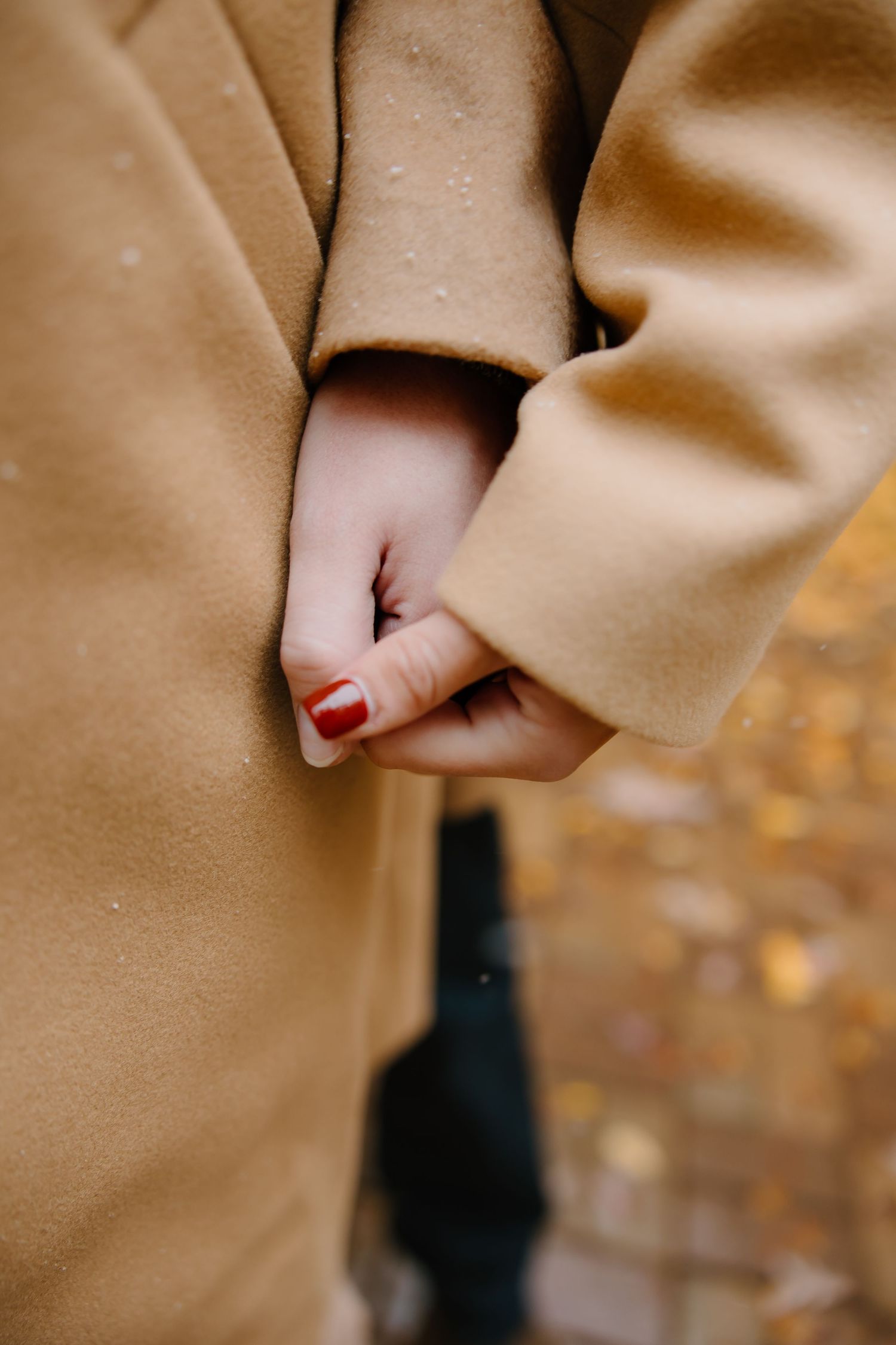 Close-up of a camel-colored coat sleeve against an autumn background.