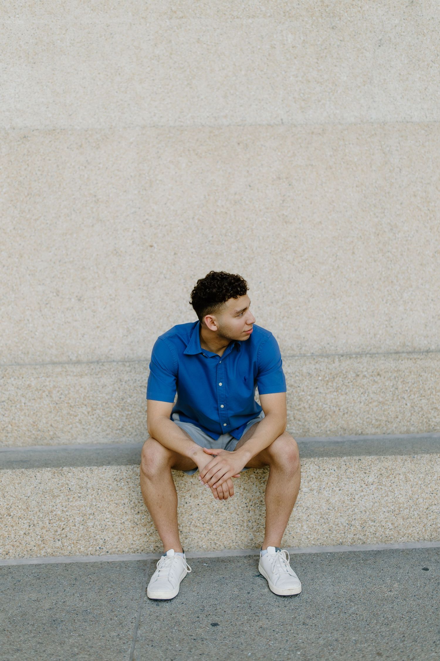 Casual portrait on concrete steps wearing a blue polo shirt and white sneakers.