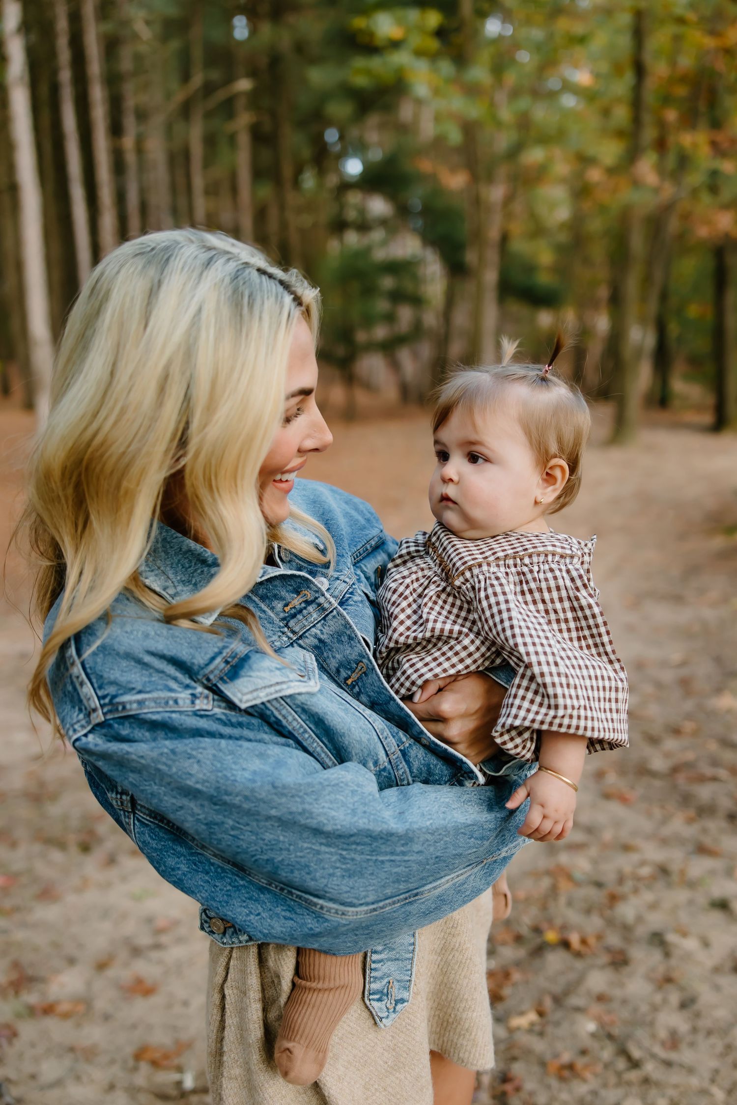 Family shares playful moments together against autumn forest backdrop wearing coordinated brown and denim outfits.