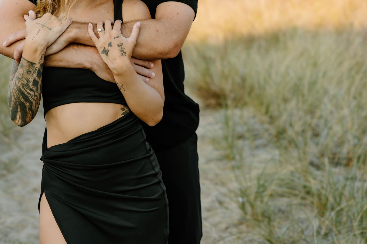 Close-up shot of a tender embrace in black outfits against golden grass.