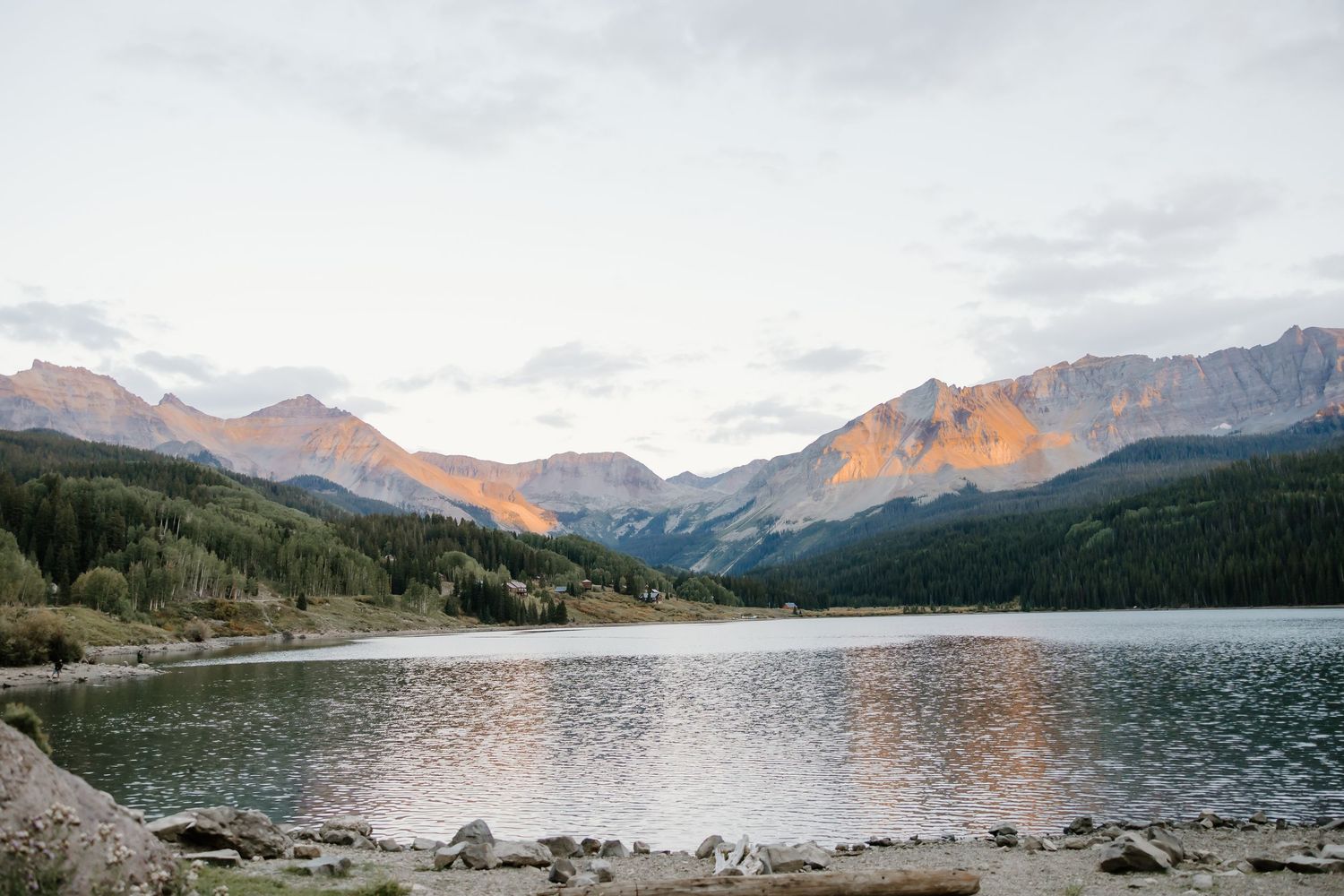 Panoramic view of a serene mountain lake with snow-capped peaks and forested shores.