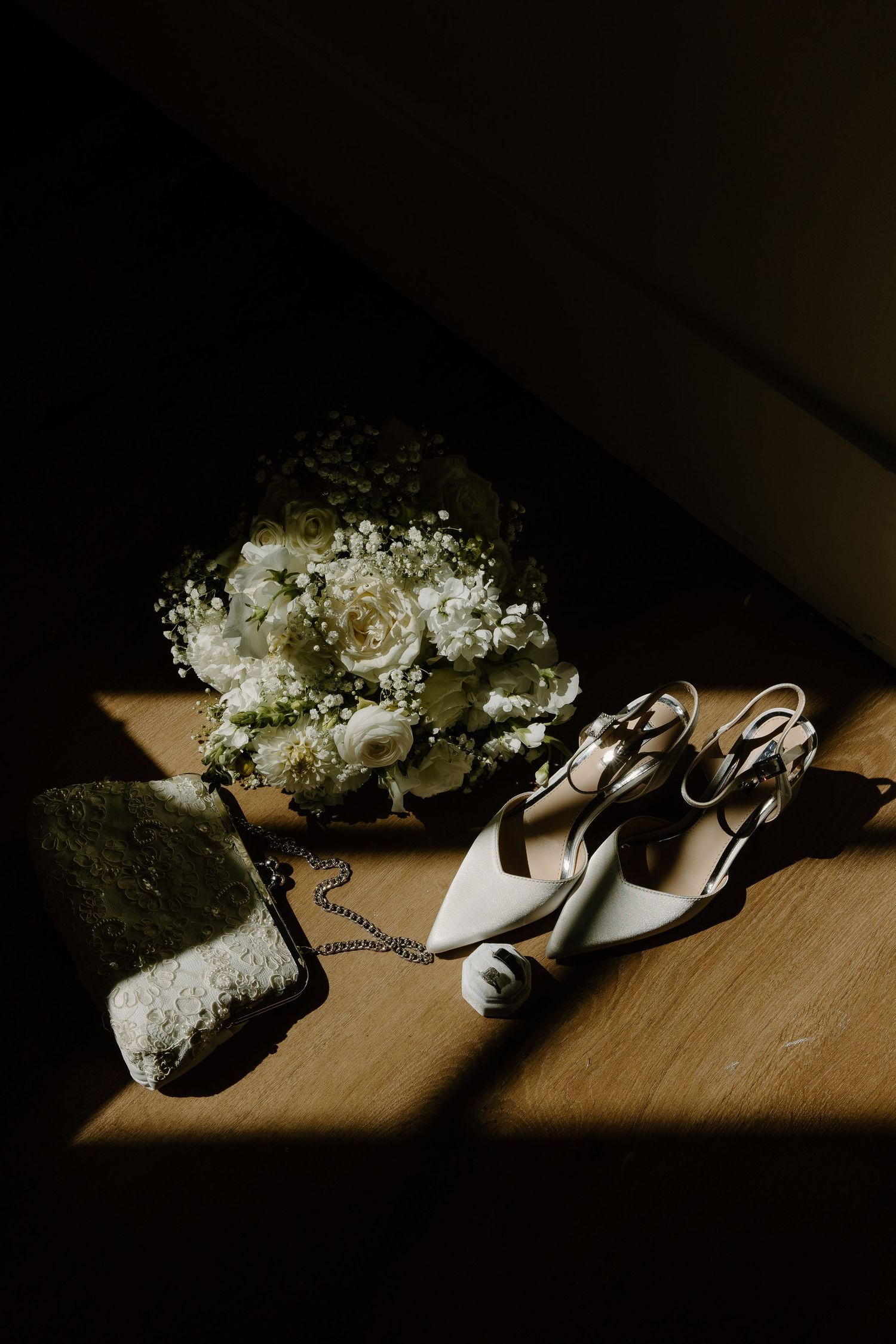 Artistic composition of bridal shoes and flowers in dramatic lighting.