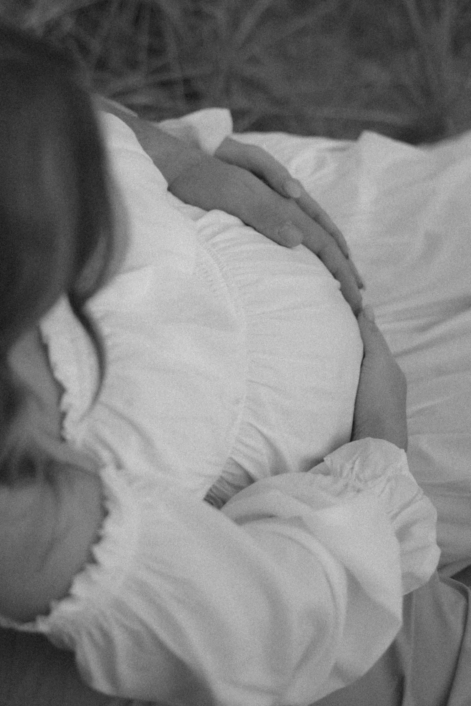 Black and white photo of a pregnant woman in a white dress cradling her baby bump with both hands.