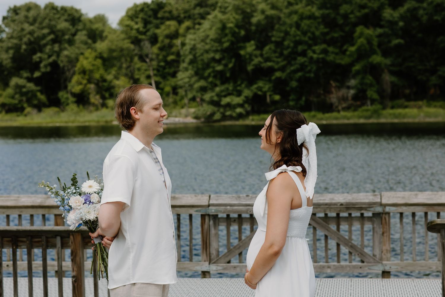 A couple shares a joyful moment on a lakeside dock during their wedding celebration.
