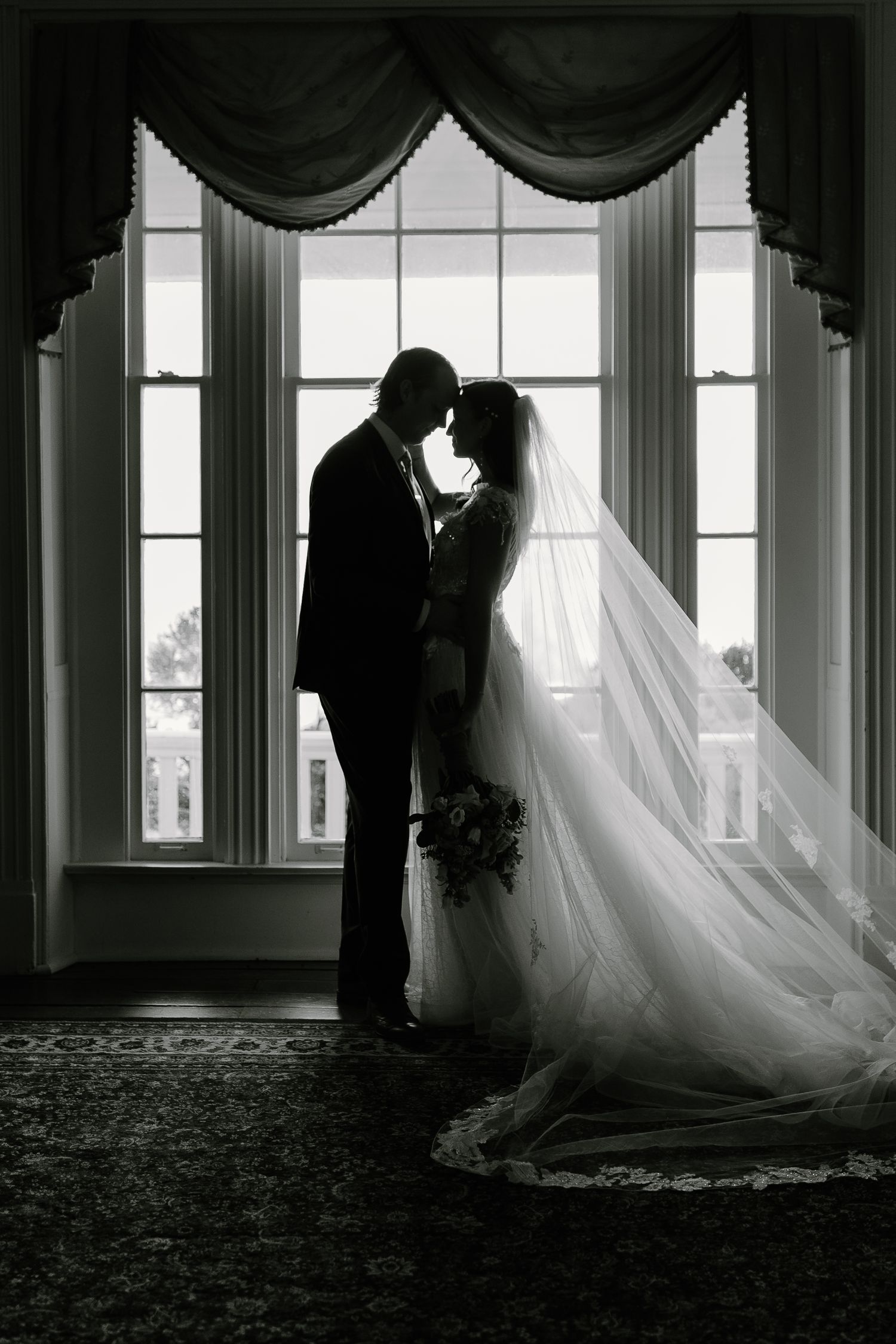 Dramatic silhouettes of a wedding couple against bright windows in an elegant room.