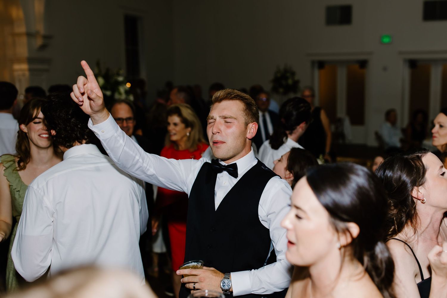 Wedding reception dance floor filled with joyful guests dancing with hands in the air.