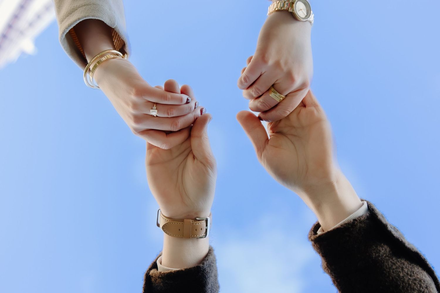 Close-up detail of hands with engagement rings against a light background.