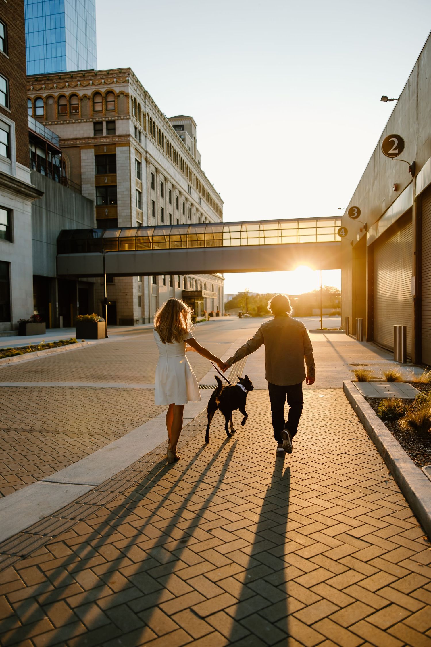 Couple walking into sunset casting long shadows on patterned pavement.