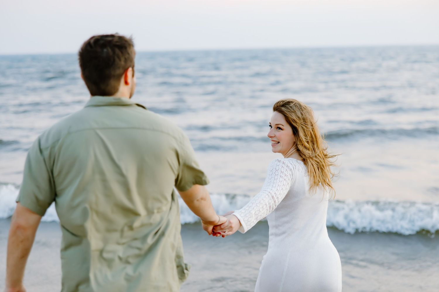 Couple walking hand in hand along the shoreline during a beach photoshoot.
