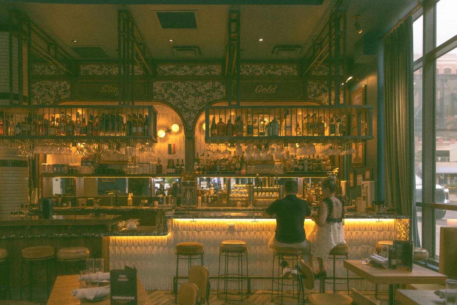 Modern bar interior with warm lighting and industrial design elements showcases hanging glass racks and exposed ceiling.
