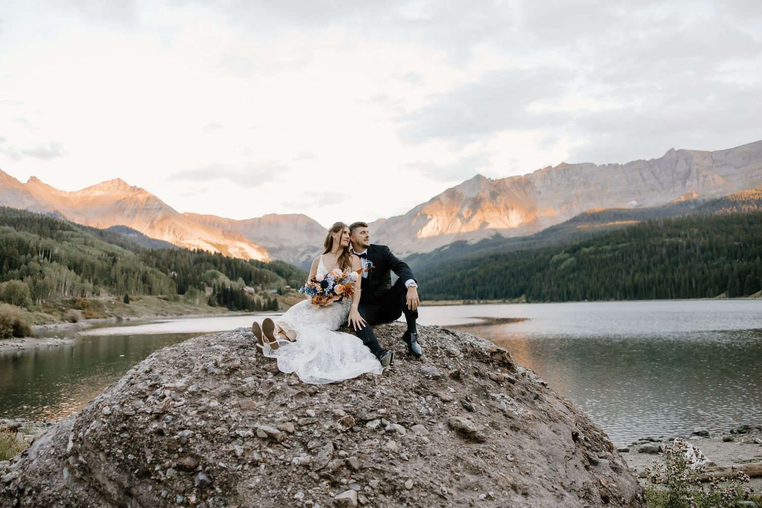 Wedding photography session on a rocky outcrop overlooking a mountain lake at sunset.
