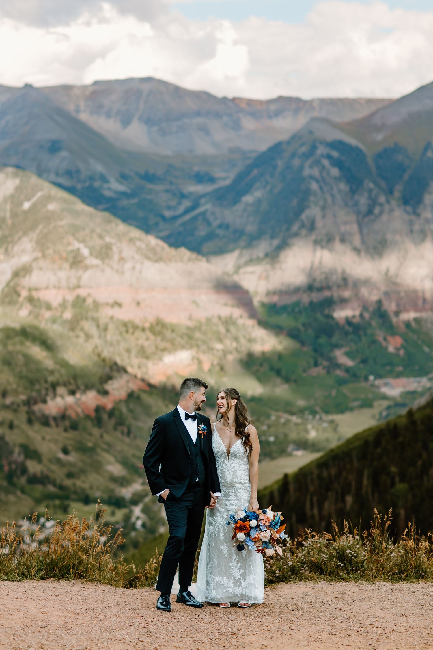 A wedding couple poses against a dramatic mountain landscape backdrop in Colorado.