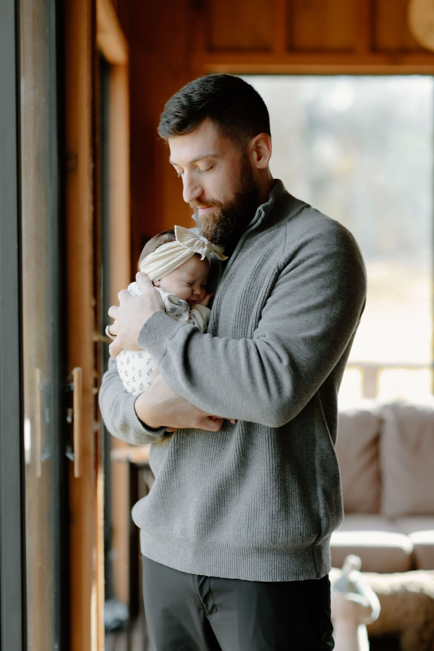 Tender moments between a parent in grey sweater holding a newborn in white.