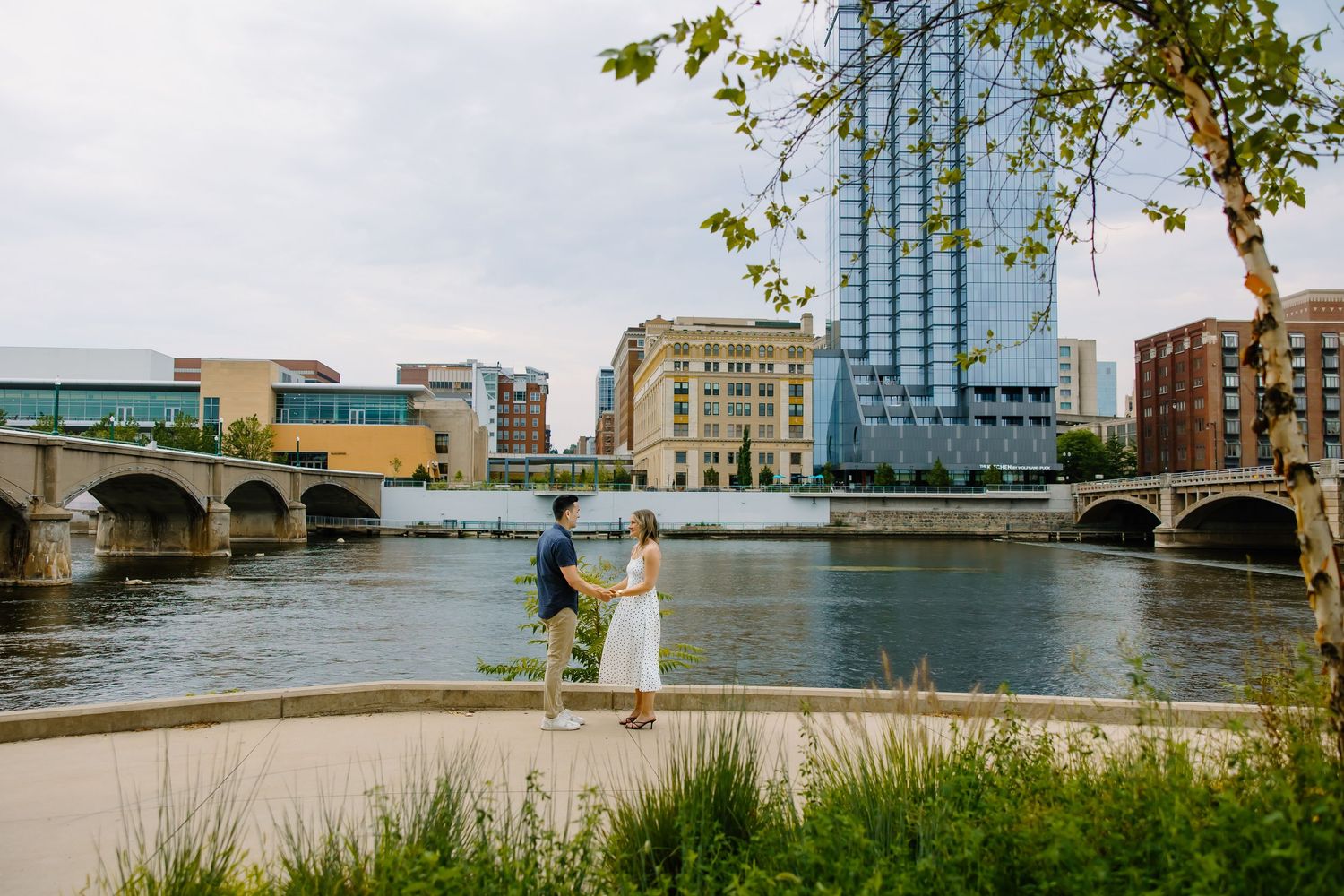 A scenic waterfront proposal scene with modern glass buildings and a bridge in the background.