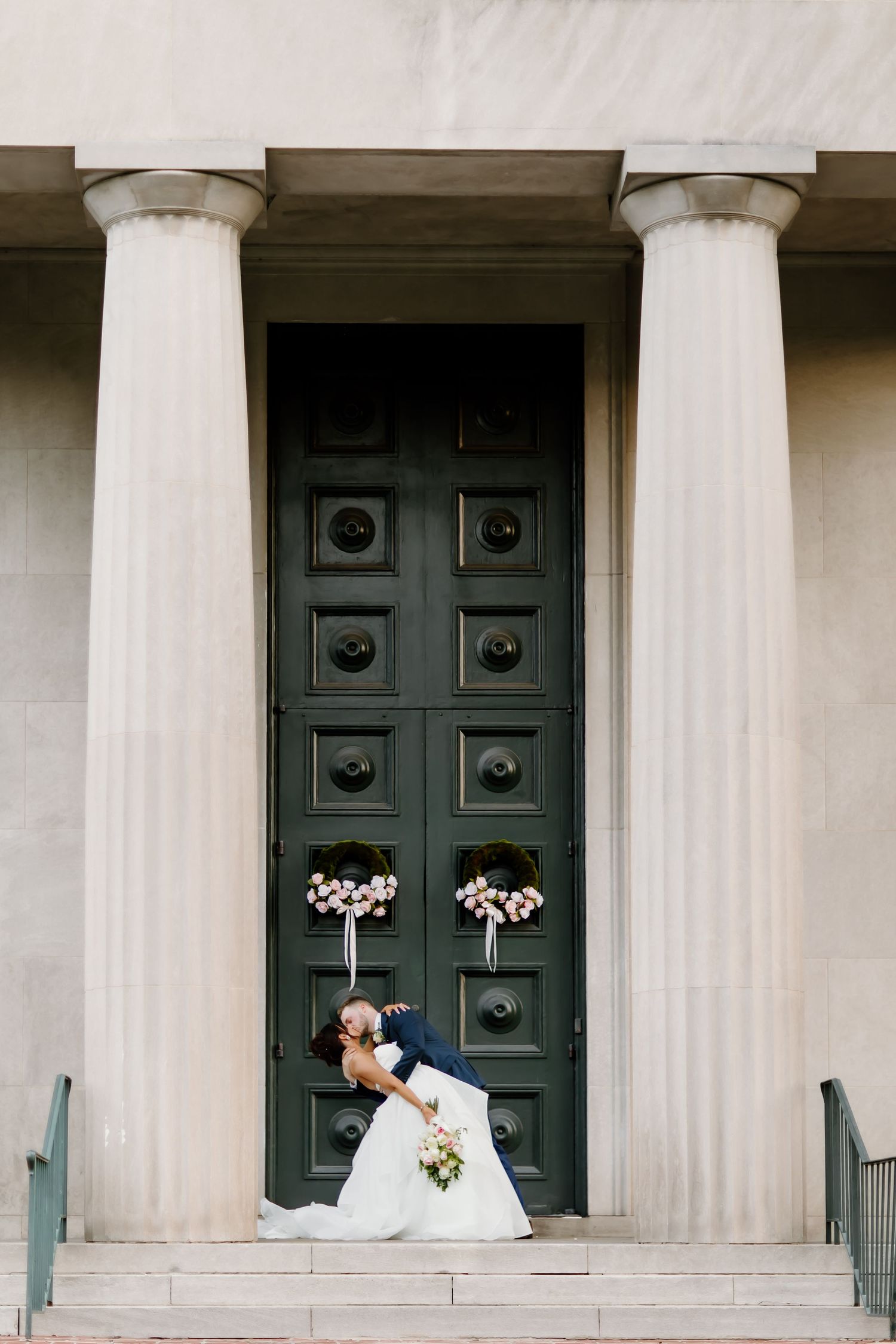 Classic brick building entrance with white columns and black doors decorated for wedding.
