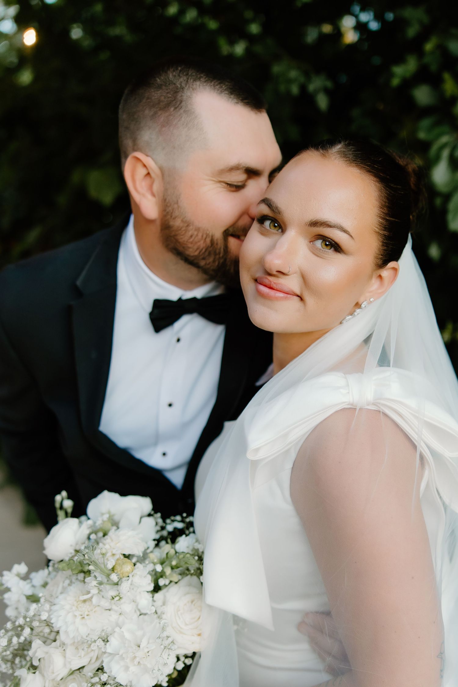 Intimate wedding portrait with white floral bouquet against greenery backdrop.