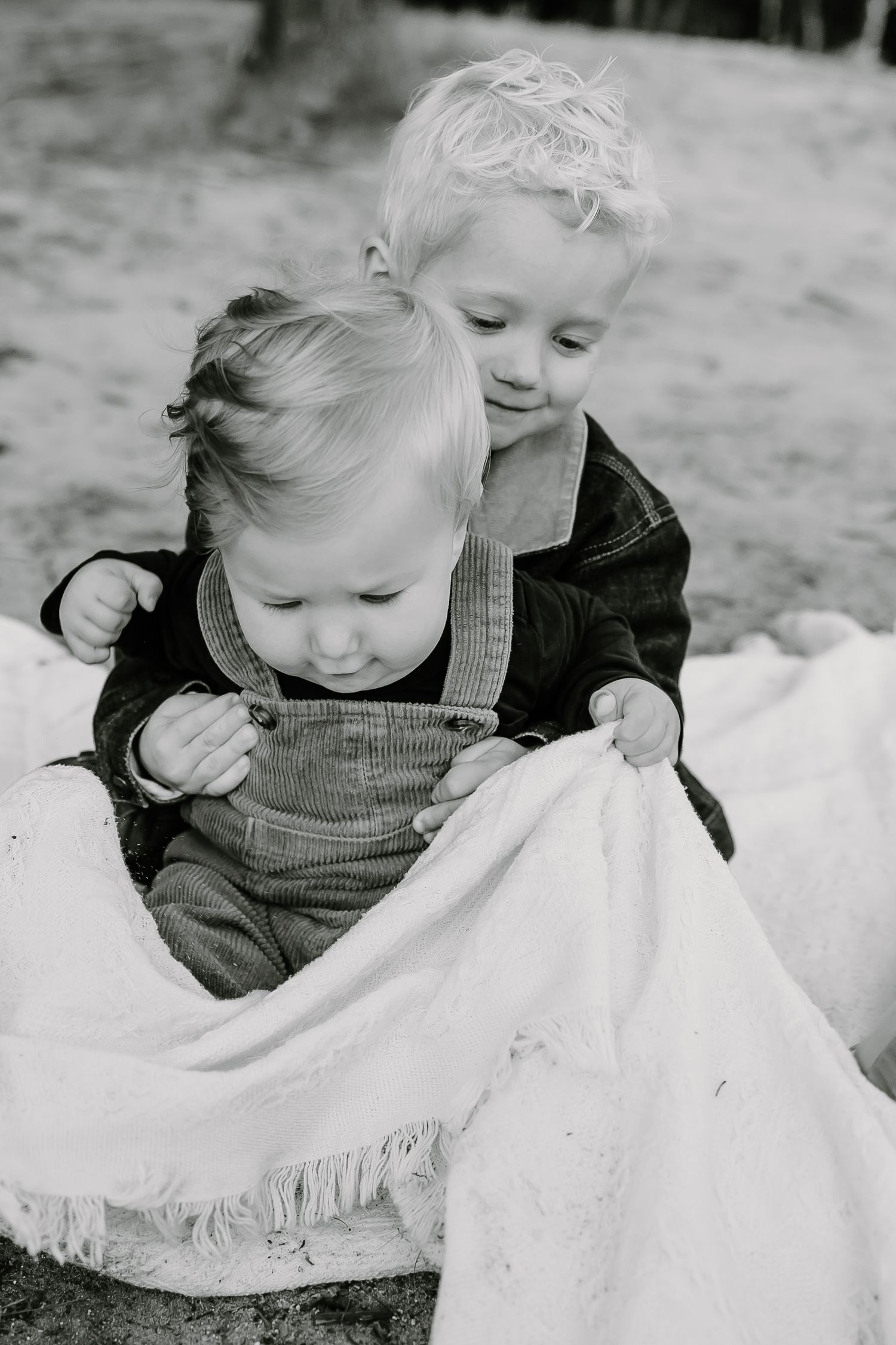 Black and white photo of a small child playing with a white blanket outdoors.