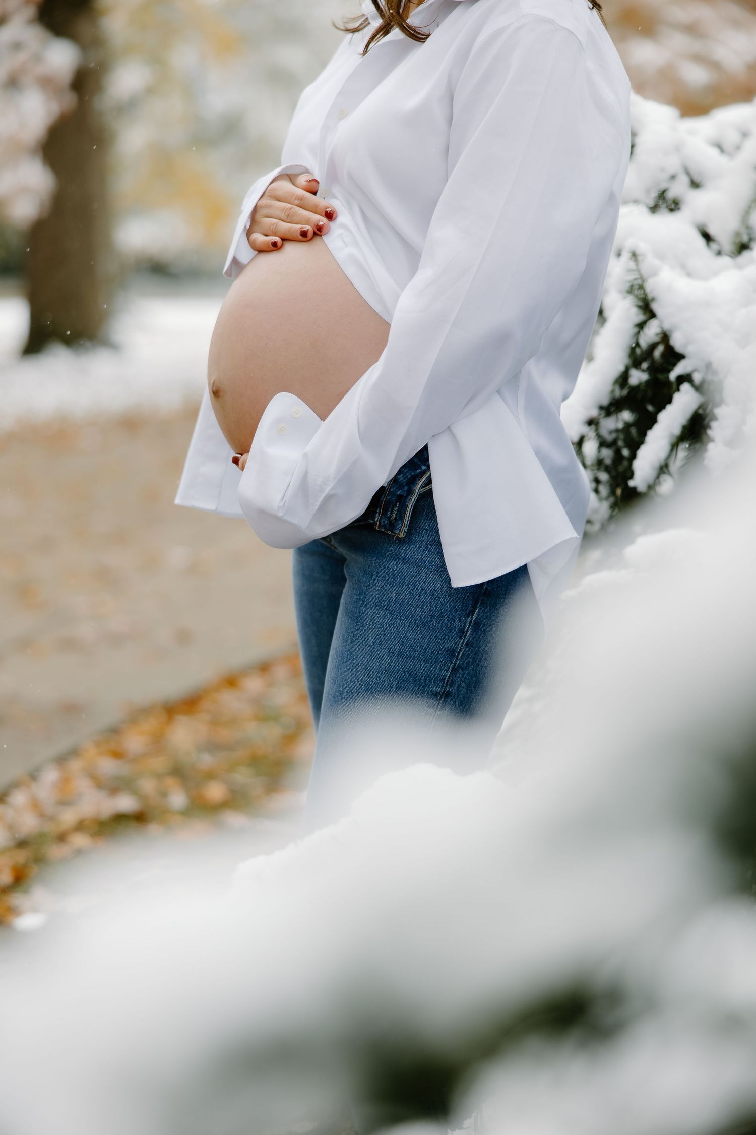 Side view of pregnant belly with white shirt against snowy winter background.