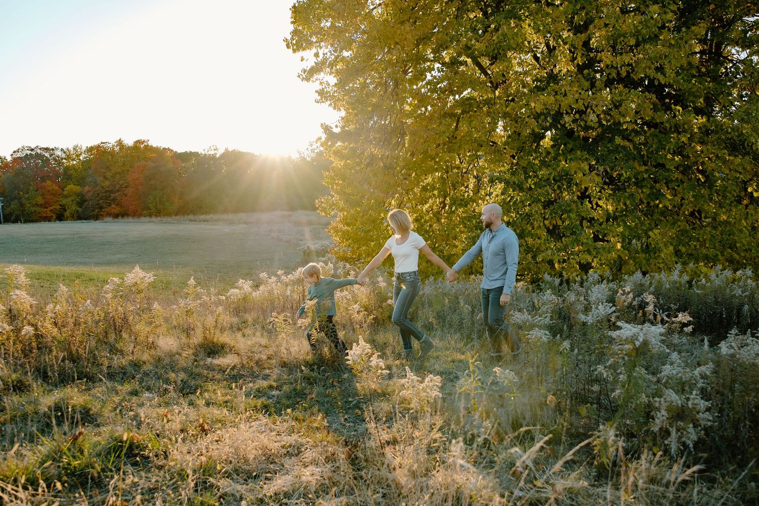 Golden sunlight illuminates a grassy field as people walk together in the distance.
