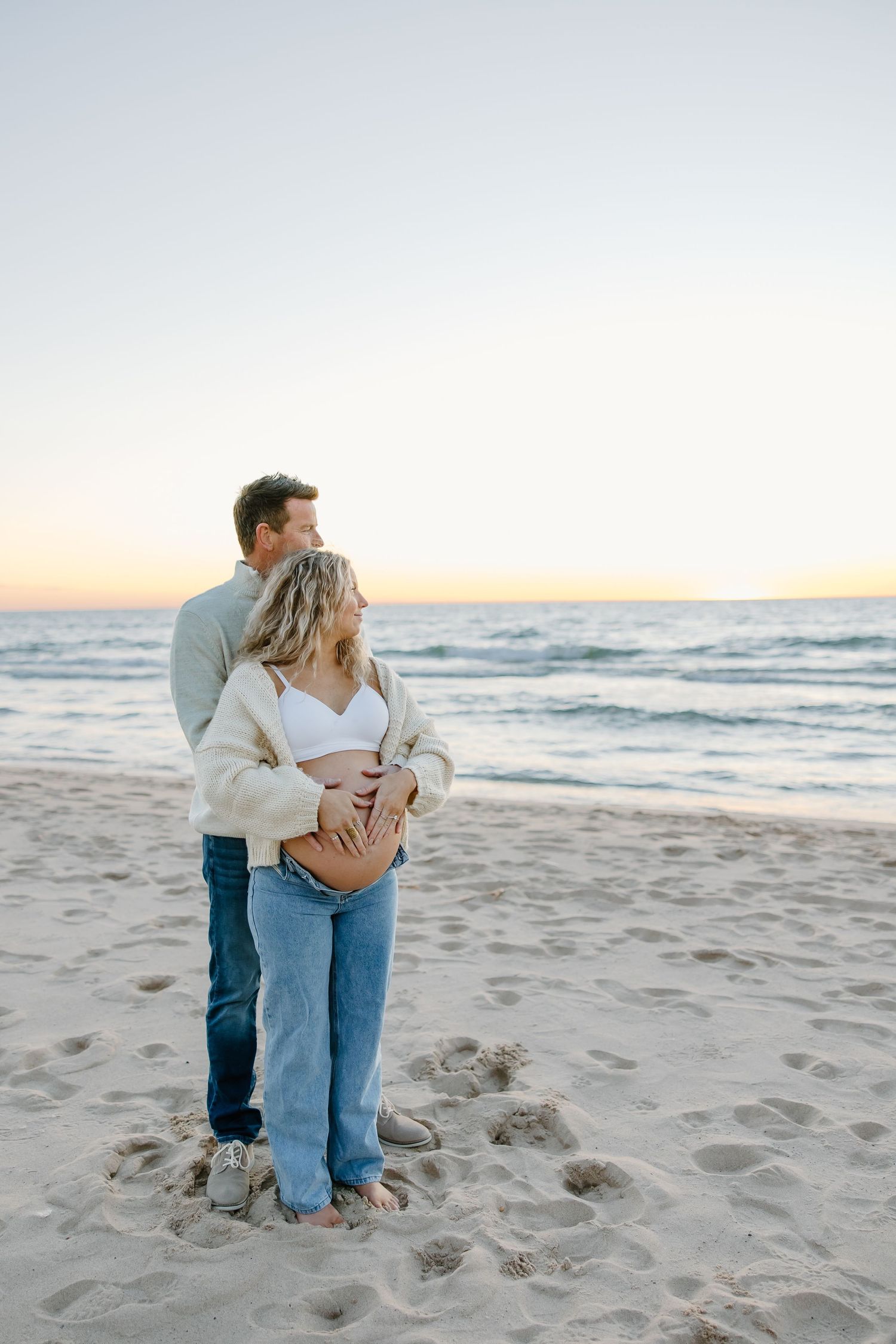 Intimate beach maternity photos with couple in jeans and cream sweaters.