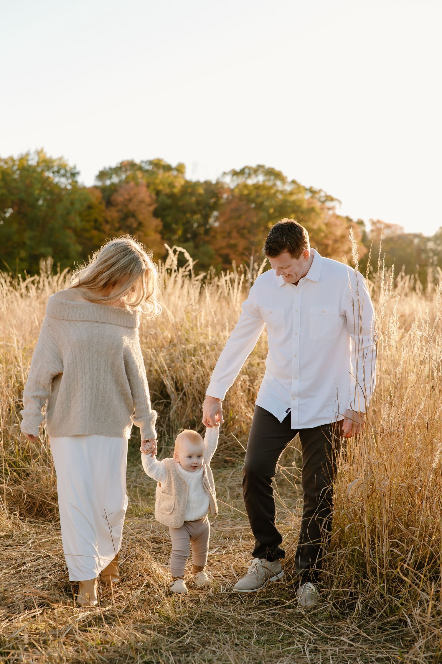 Family walking through tall golden grass at sunset in matching white outfits.