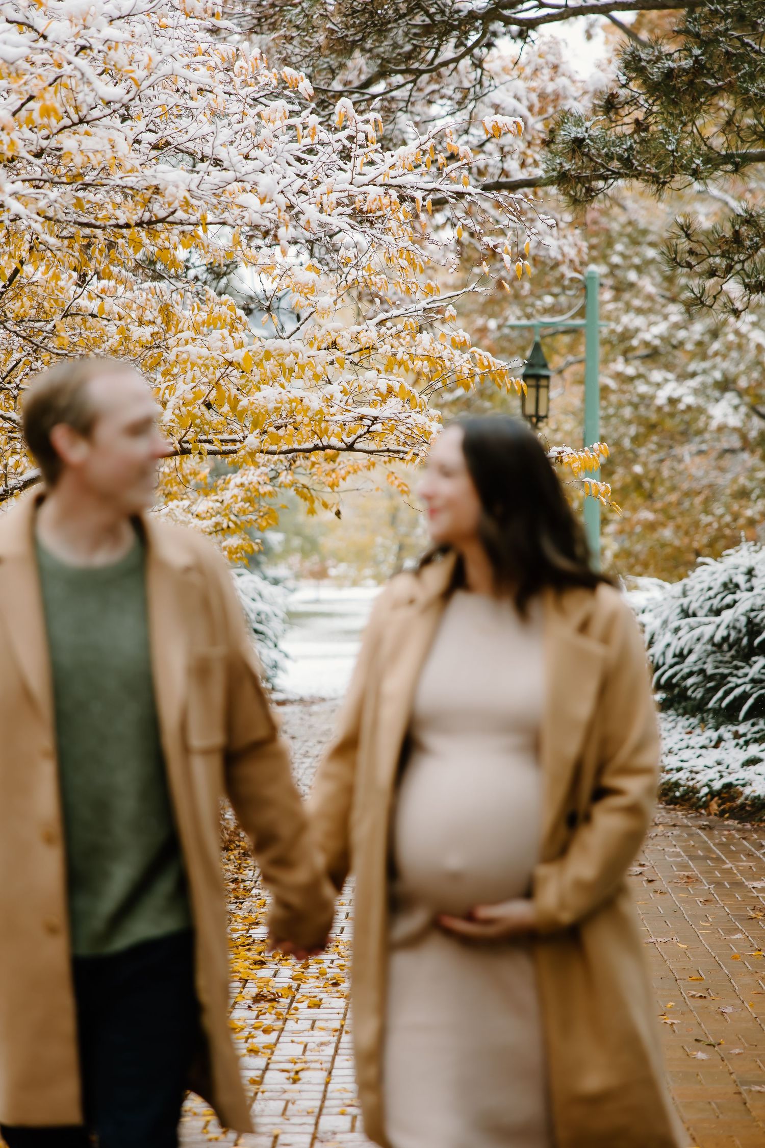Couple strolling along a tree-lined path with snow and fall foliage.